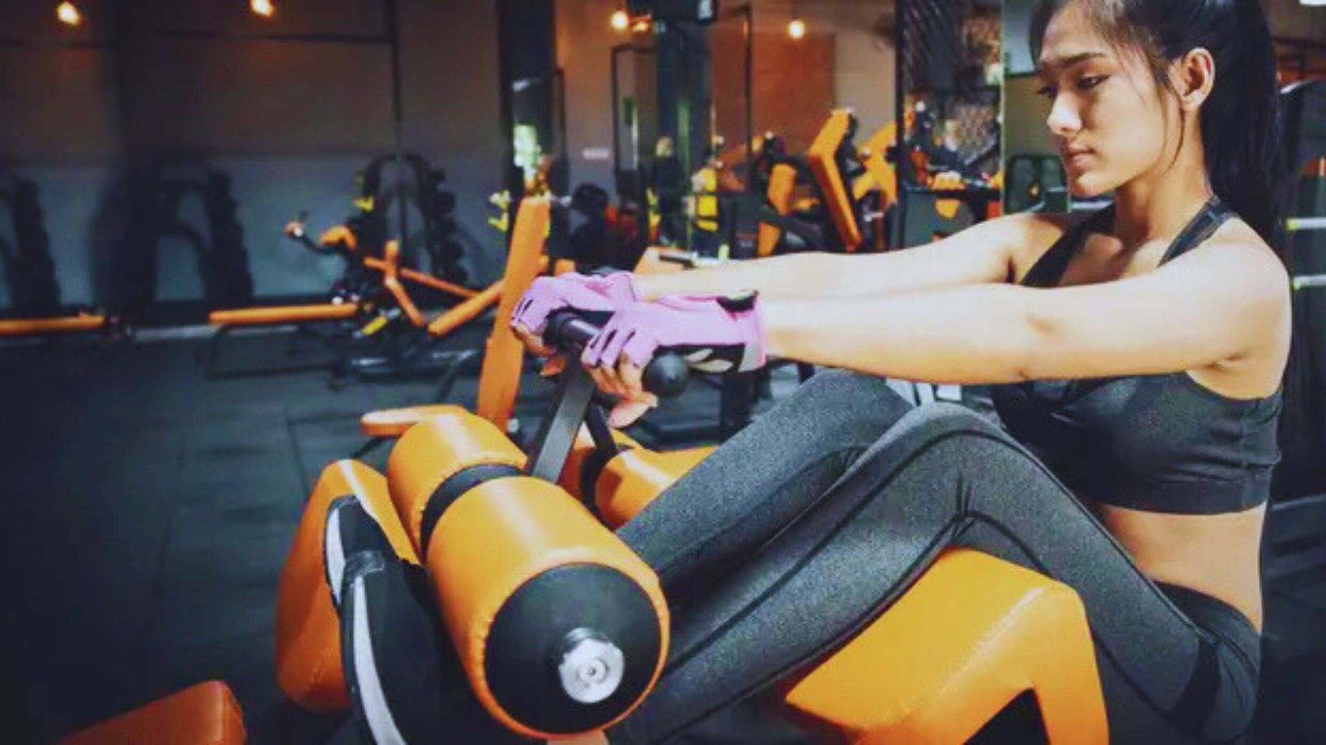 A woman sits on an exercise machine in a gym, focusing on her workout routine for abdominal strength training.