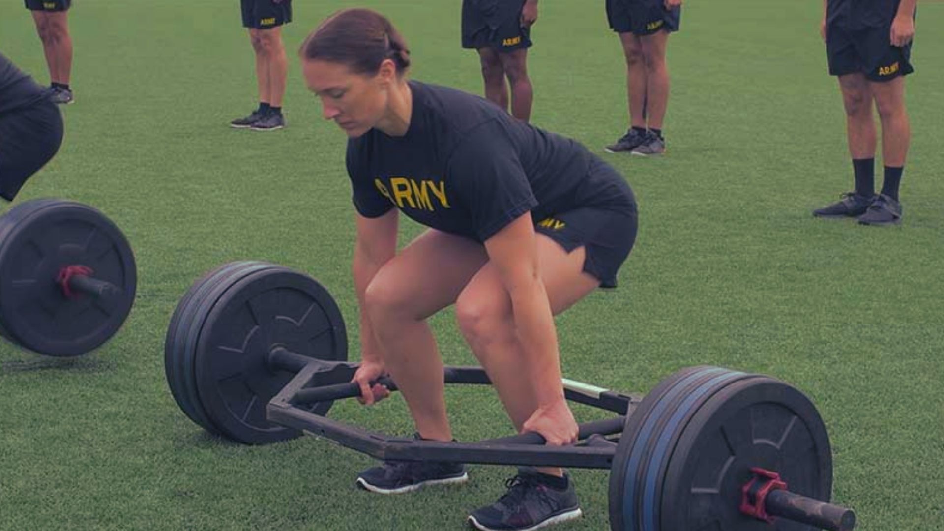 1. A woman lifts a barbell on a grassy field, demonstrating strength and fitness in an outdoor setting.