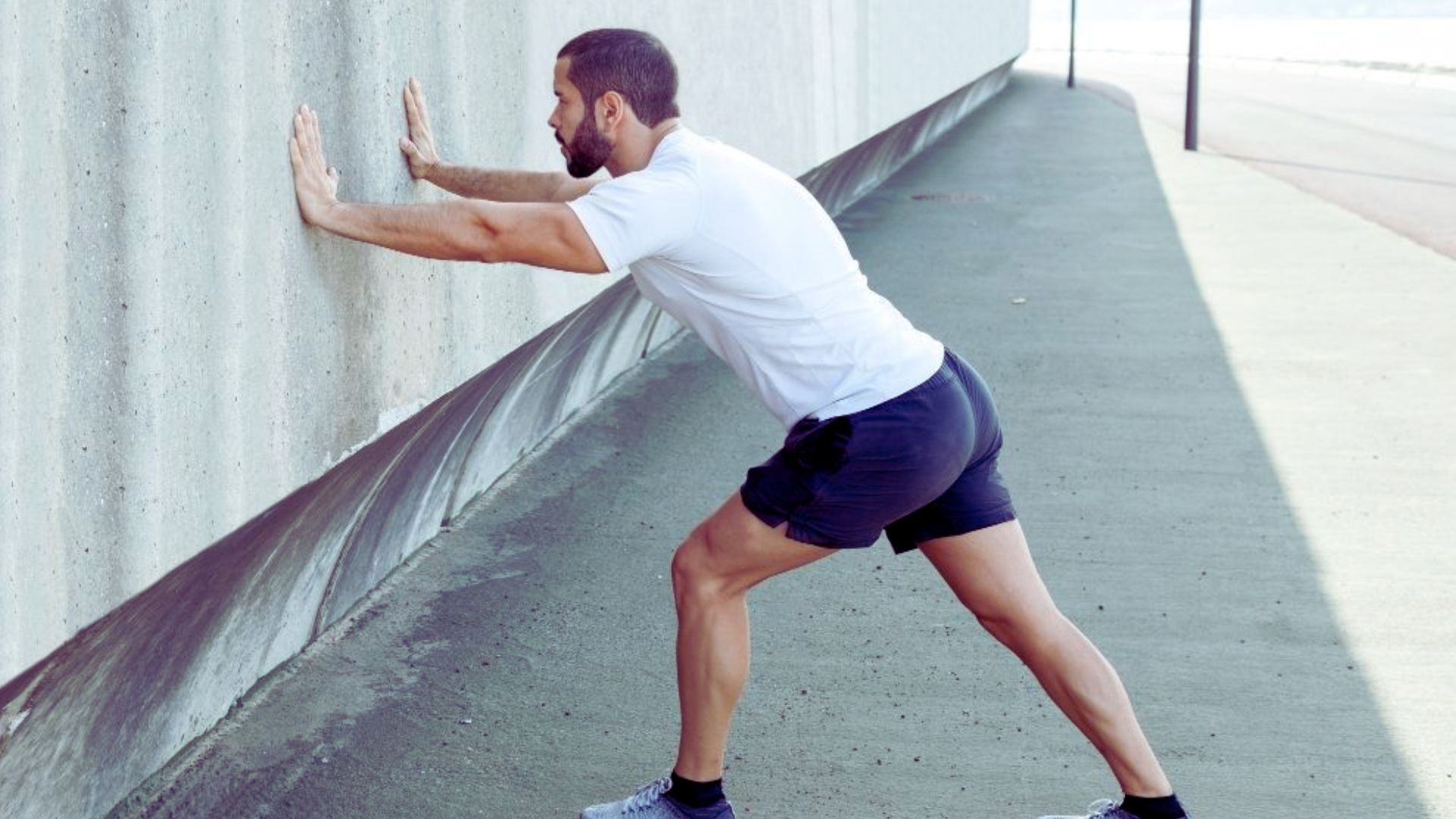 A man leans casually against a wall, with a relaxed posture and a thoughtful expression on his face.