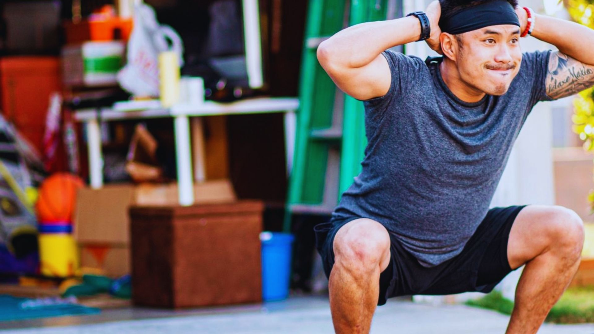 A man performs squats in front of a garage, focusing on his fitness routine in an outdoor setting.