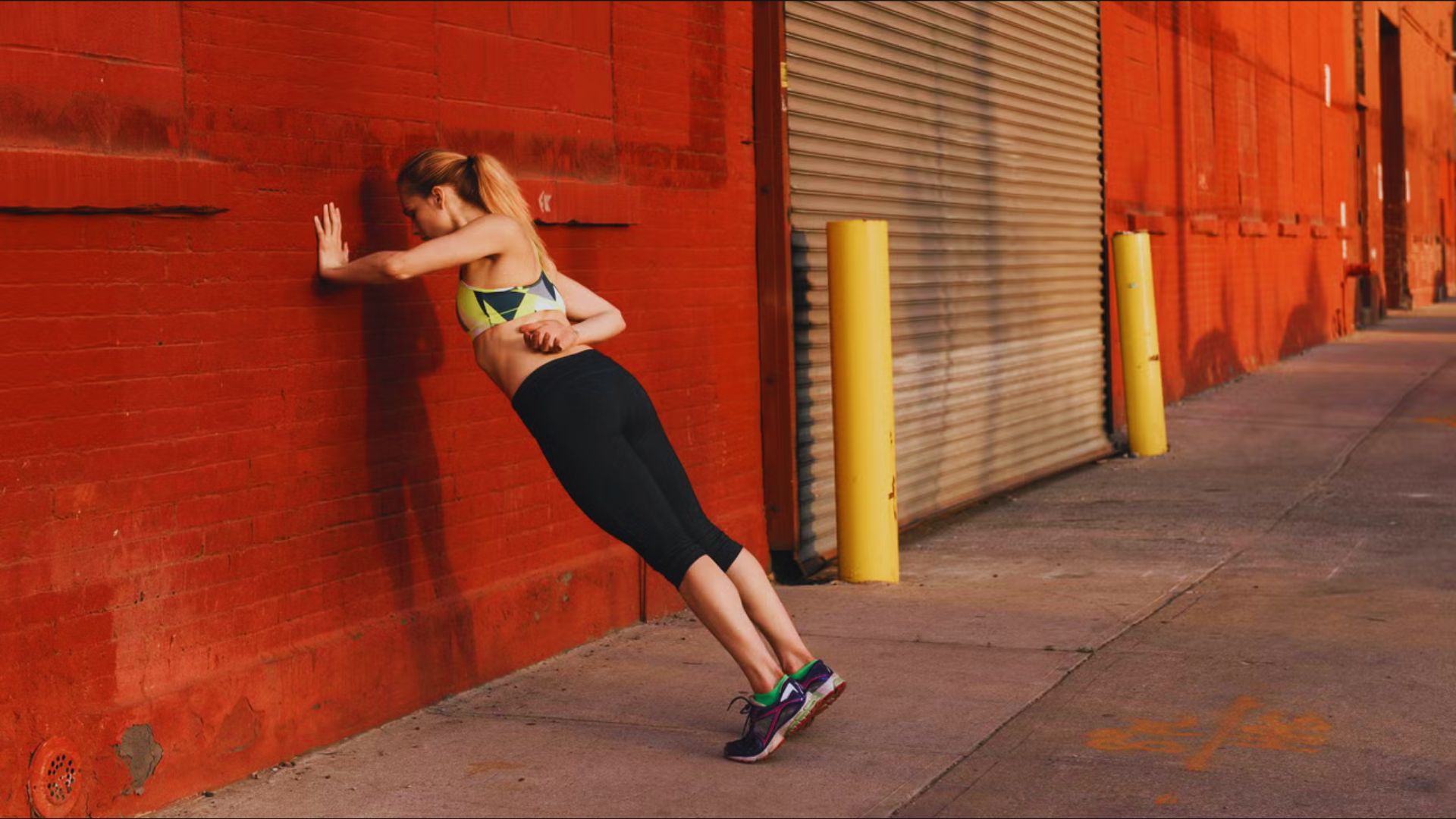 A woman leans casually against a wall, appearing relaxed and contemplative.