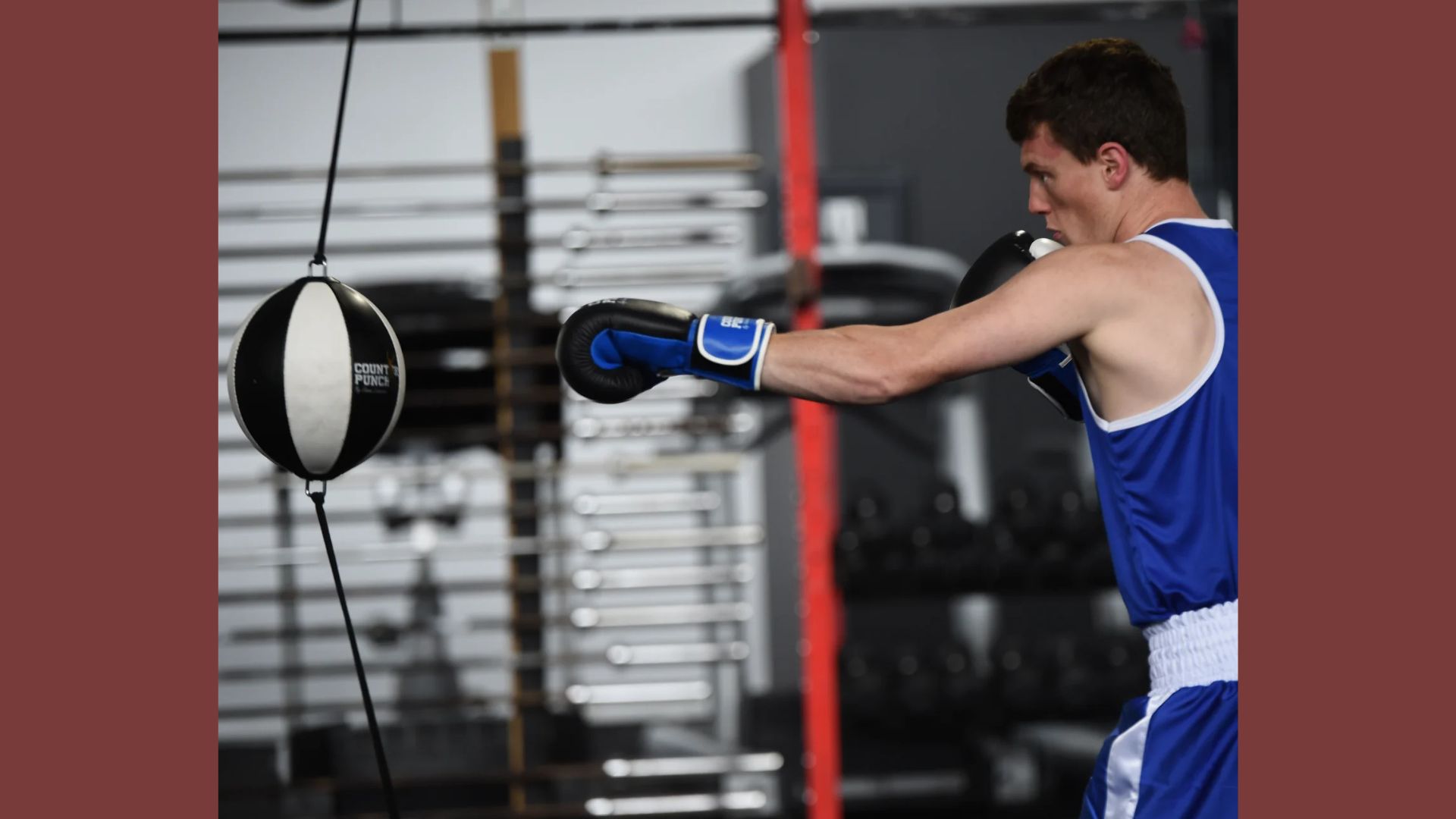 A man in blue boxing gear strikes a punching bag with focused intensity during a training session.