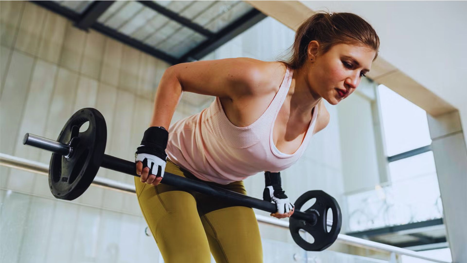 A woman is lifting a barbell while exercising in a gym, demonstrating strength and focus.
