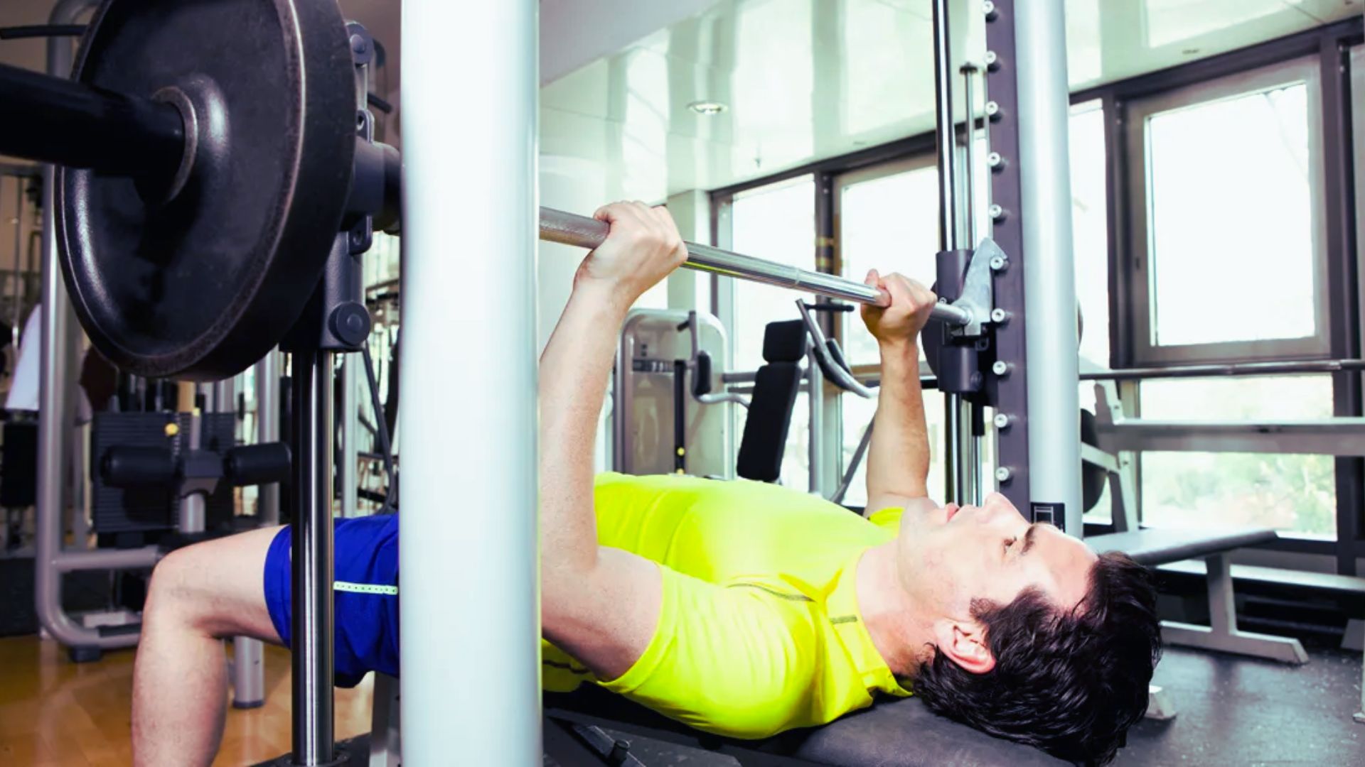 A man performs a bench press exercise in a gym, focusing on lifting a barbell above his chest.