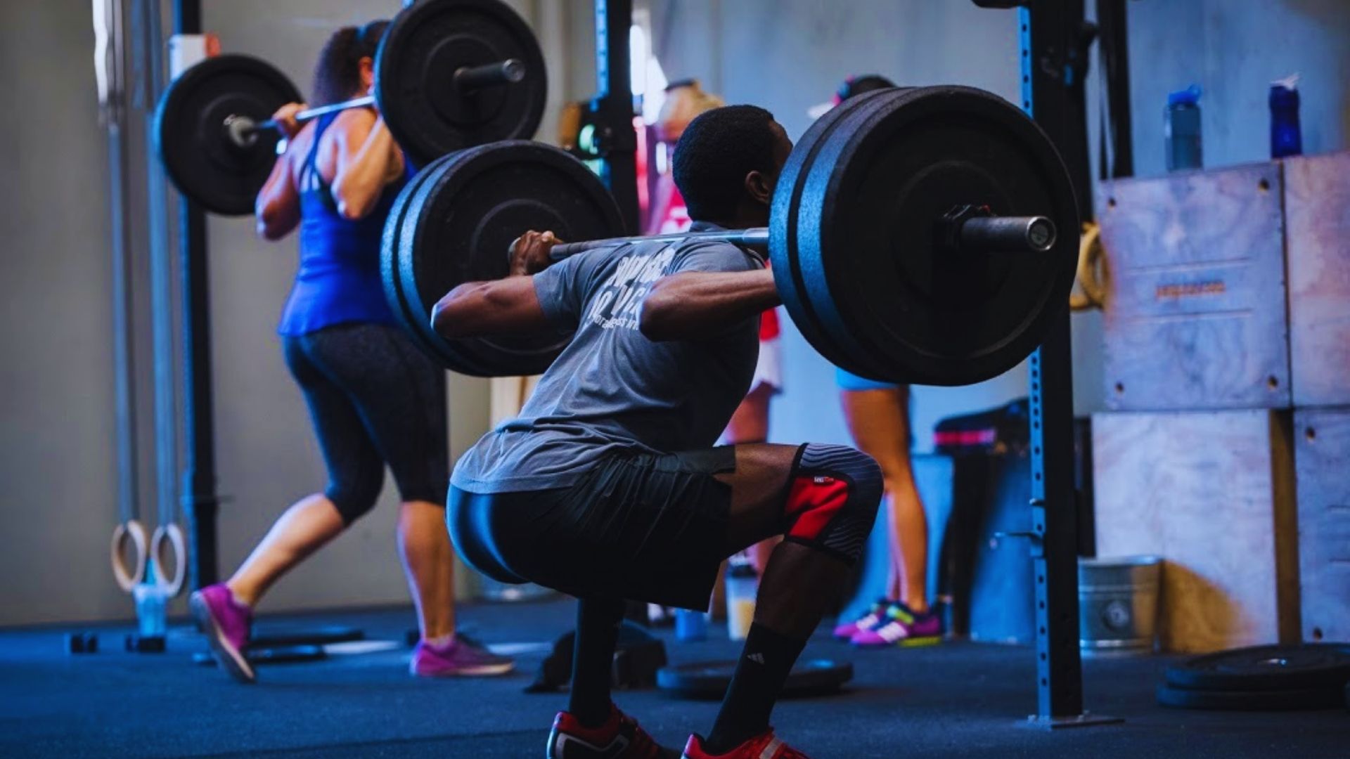 A man performs a squat with a barbell in a gym, demonstrating proper weightlifting technique and concentration.