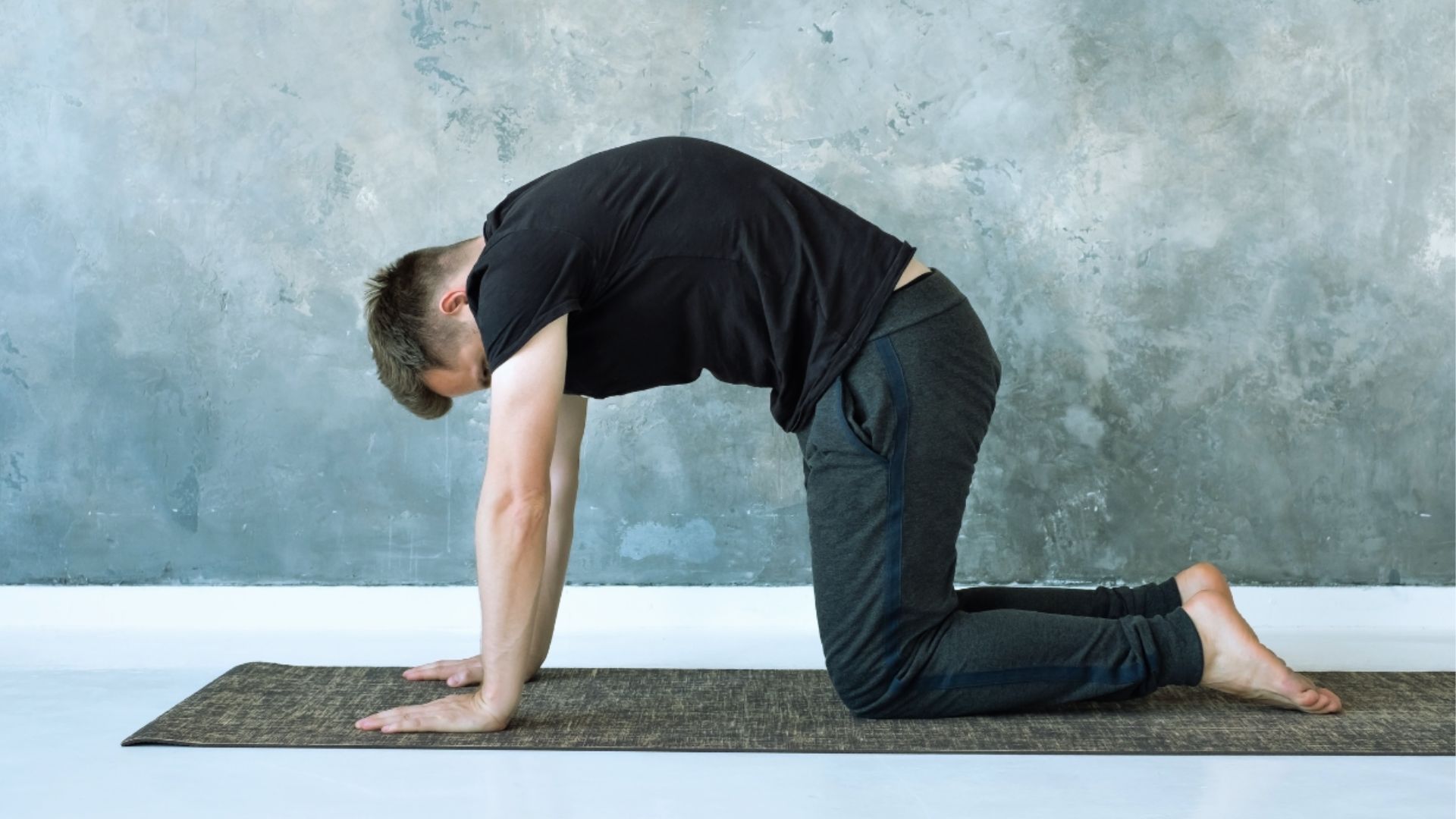 A man performs a downward bend on a yoga mat, focusing on his flexibility and balance during the exercise.