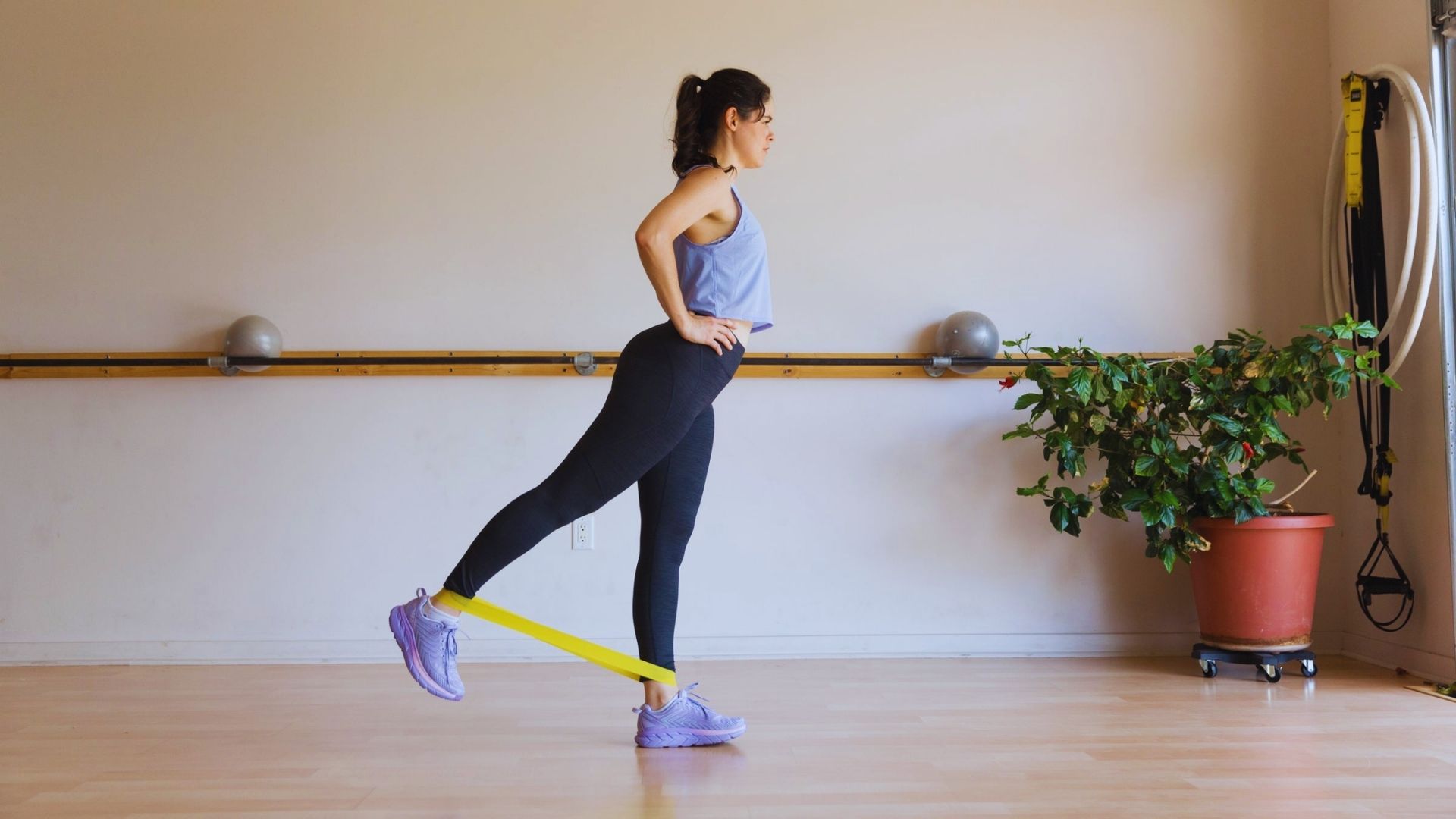 A woman performs a resistance band exercise, focusing on strength training and fitness in a bright gym setting.