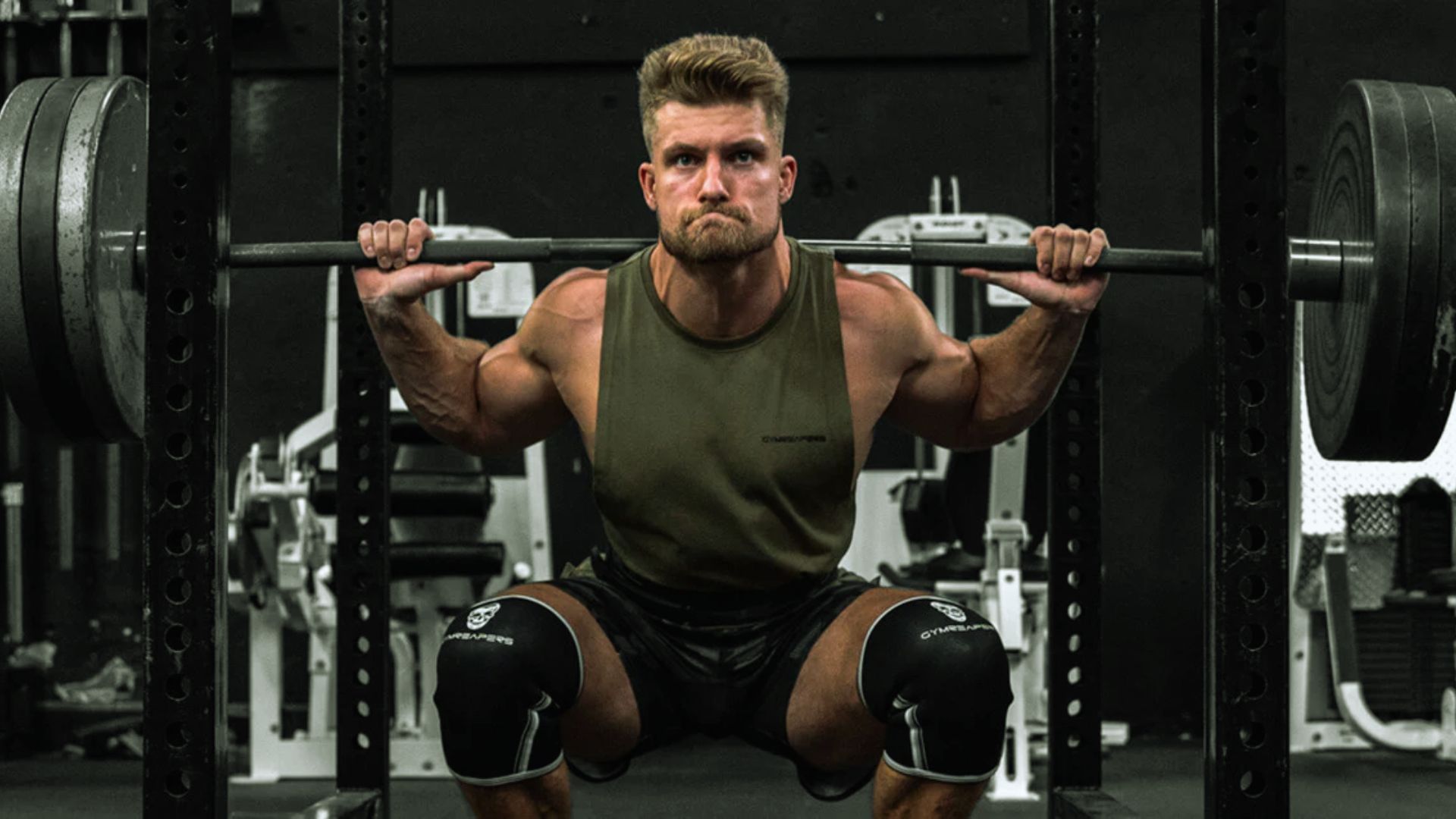 A man squats with a barbell in a gym, focusing on strength training and proper form.