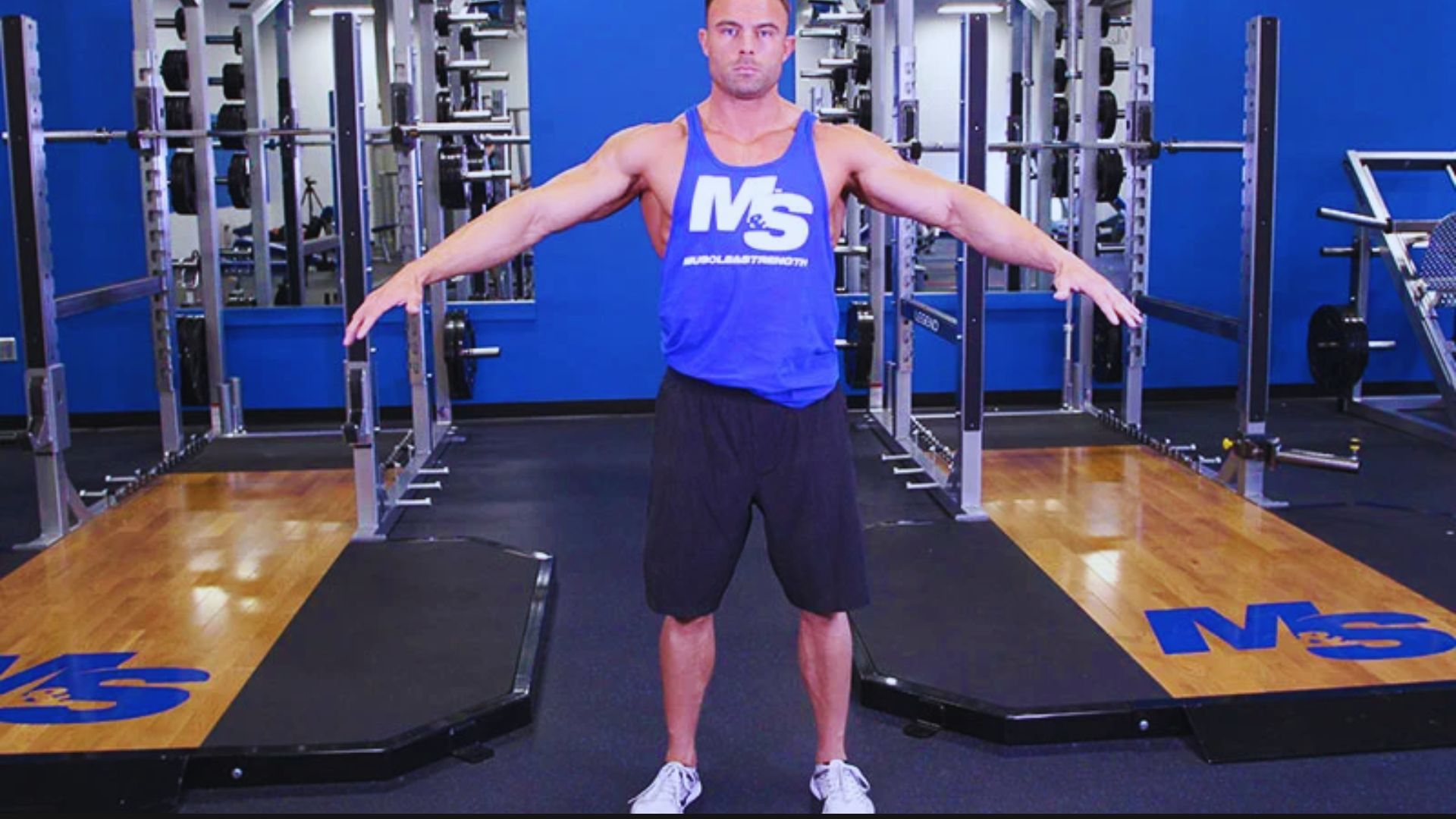 A man in a blue tank top performs a push-up on a gym floor, focusing on his form and strength.