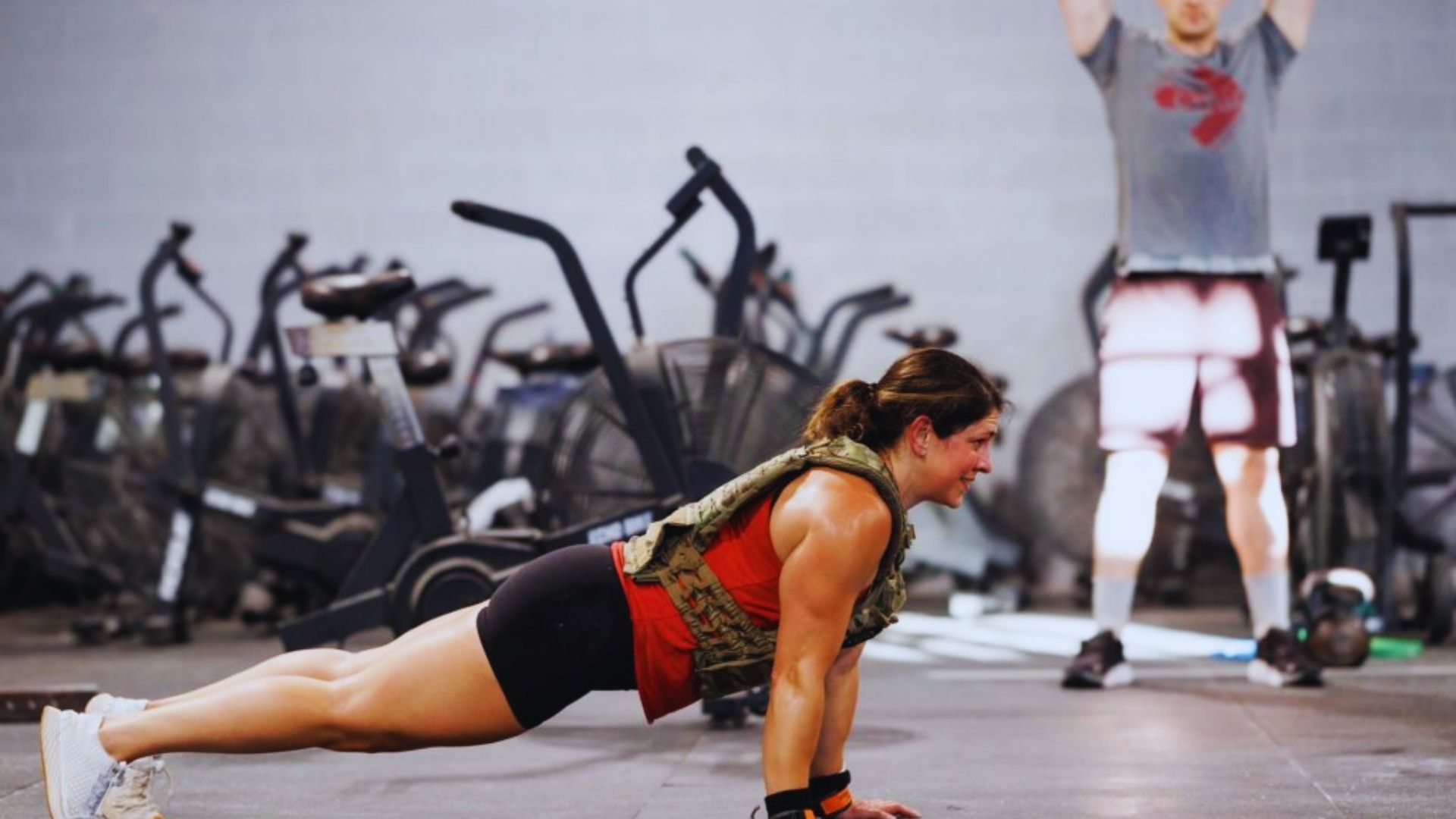A woman performing push-ups on a gym mat, focused and determined, with gym equipment visible in the background.