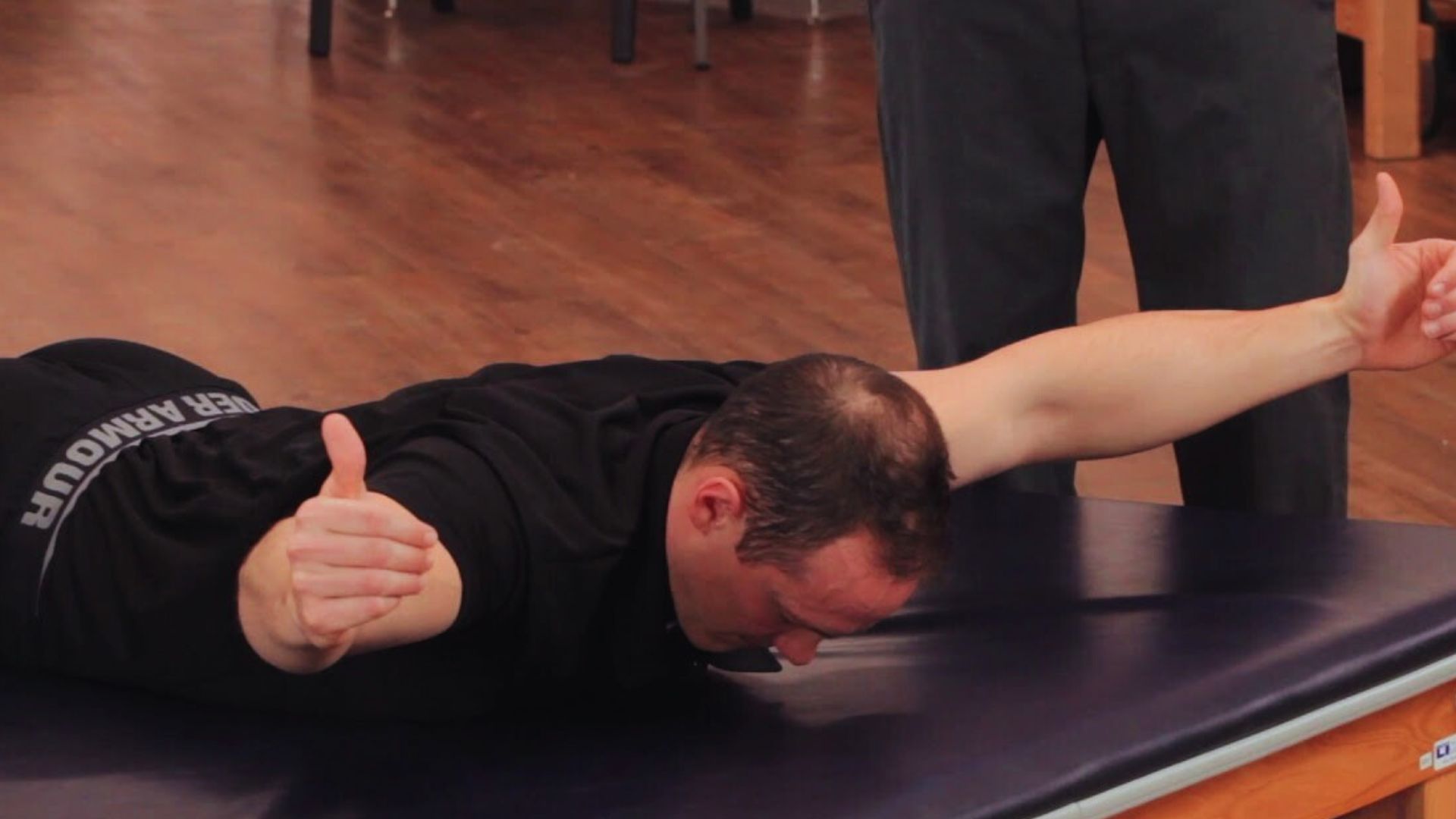 A man lies on a table with his hands raised above his head, appearing relaxed and at ease.