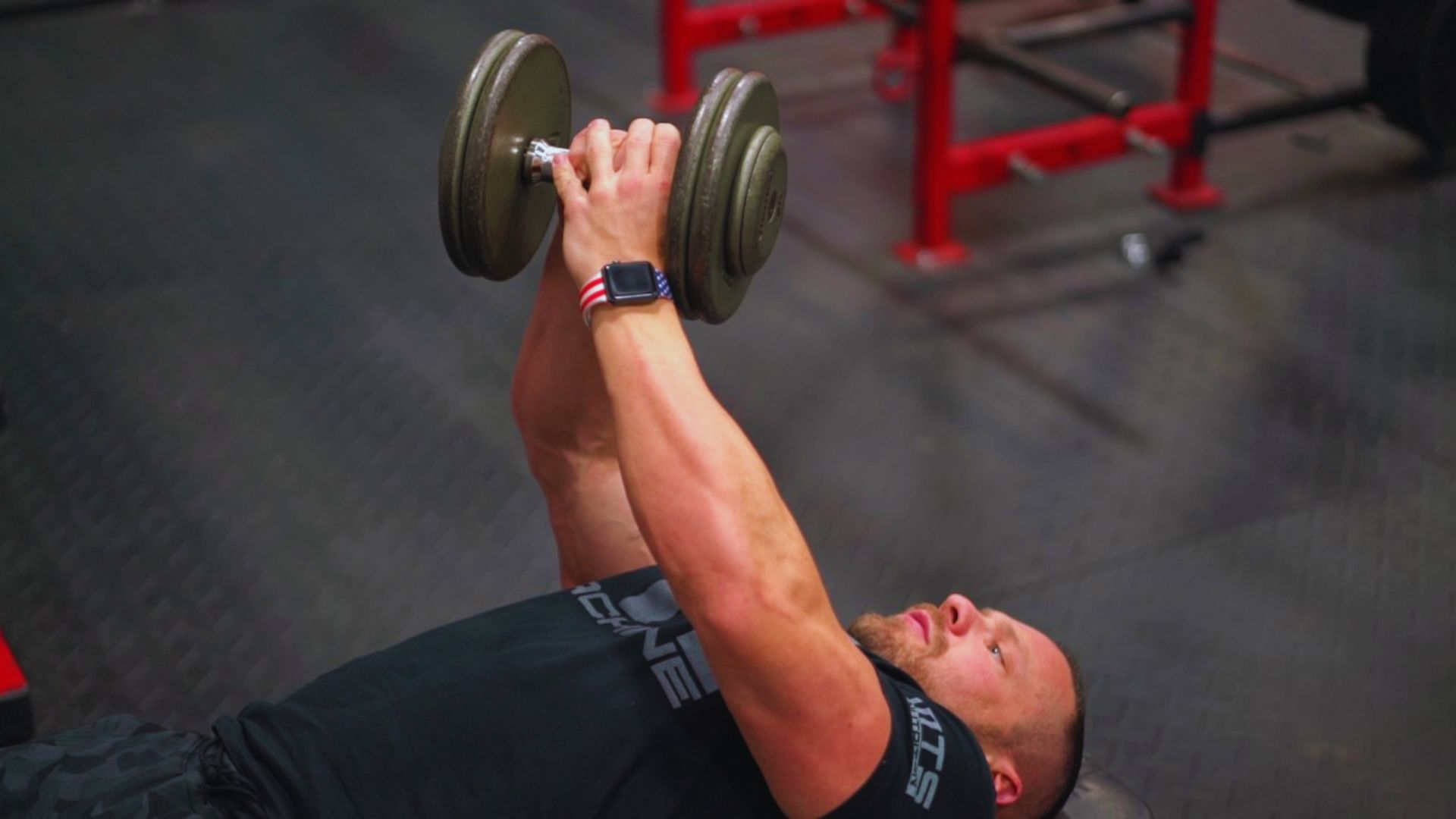 A man lifts a dumbbell while exercising in a gym, focusing on strength training.