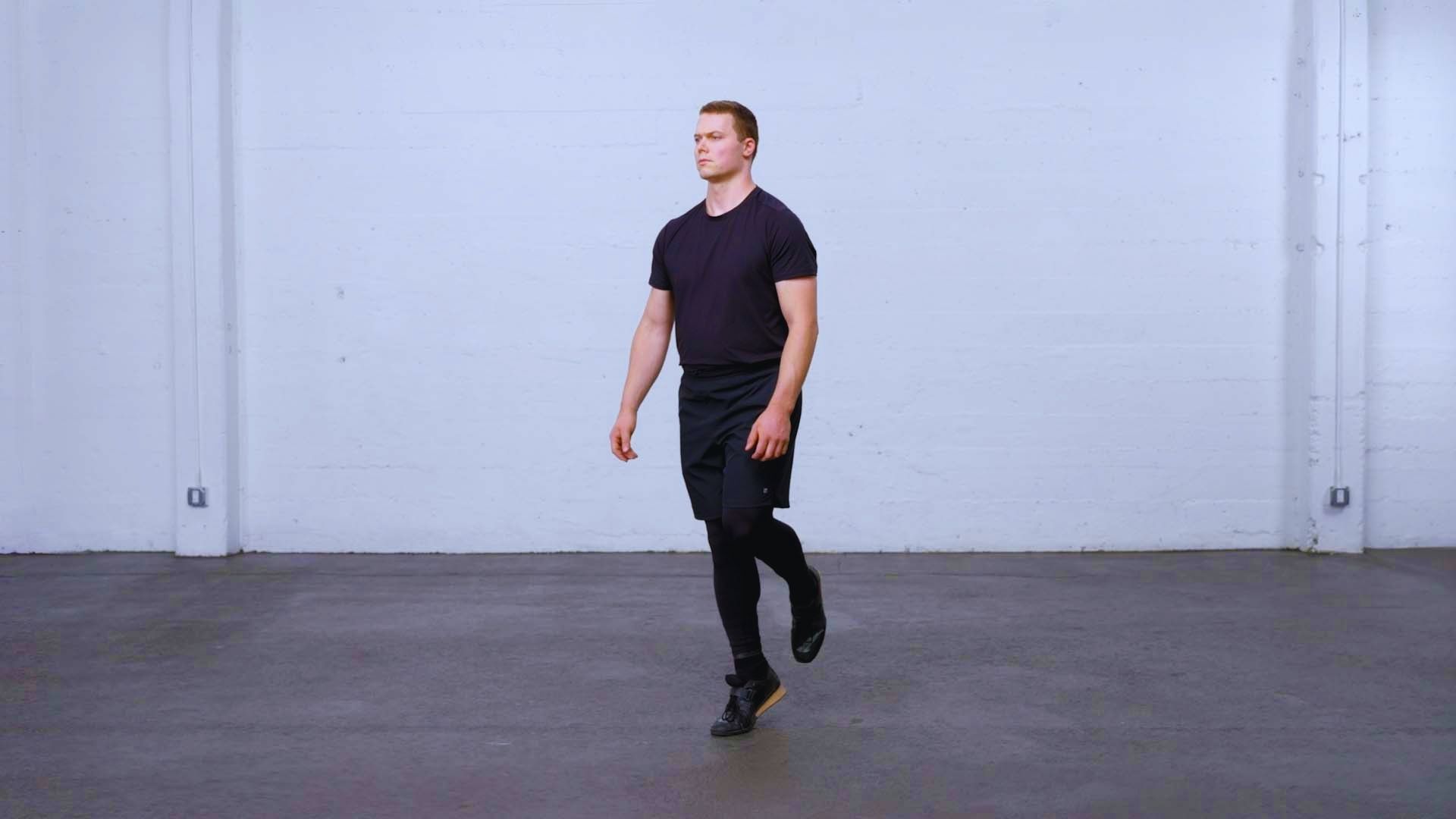A man wearing a black shirt and black shorts is walking along a path.