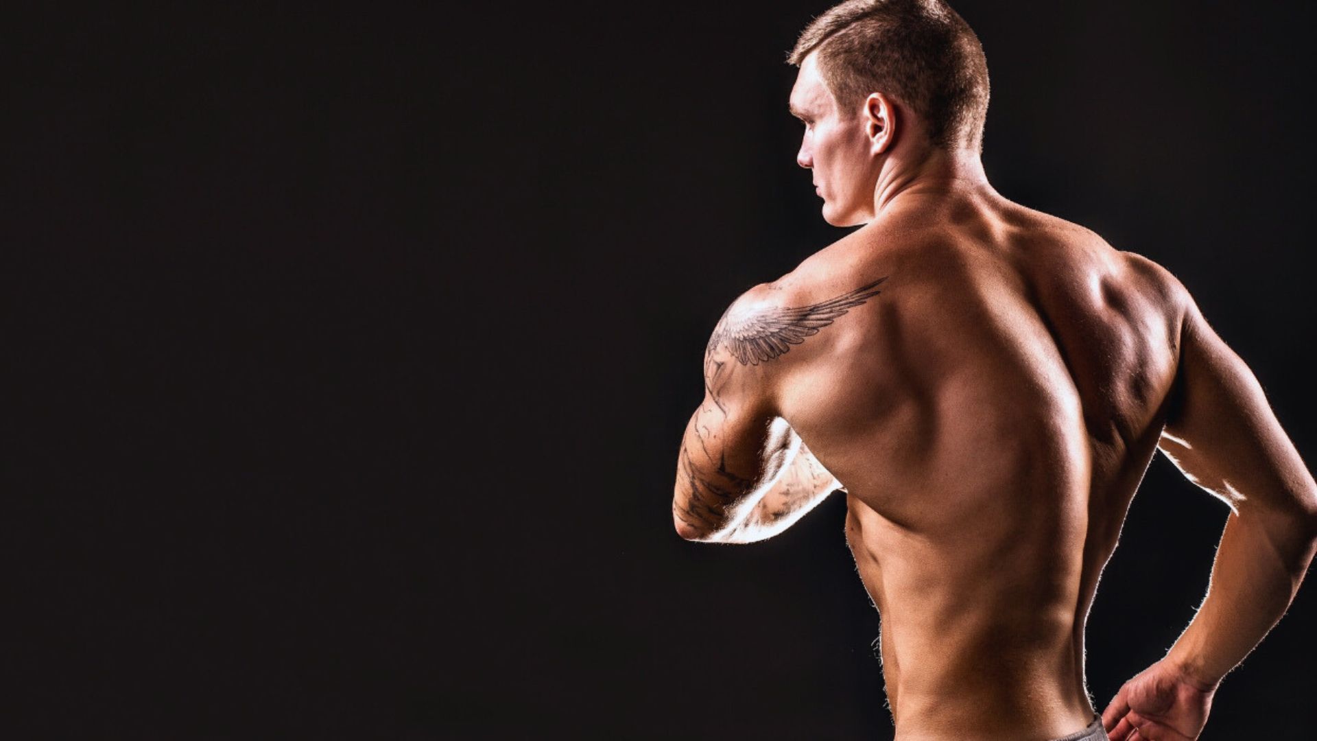A man displays his tattooed back and arms, showcasing intricate designs and vibrant colors.