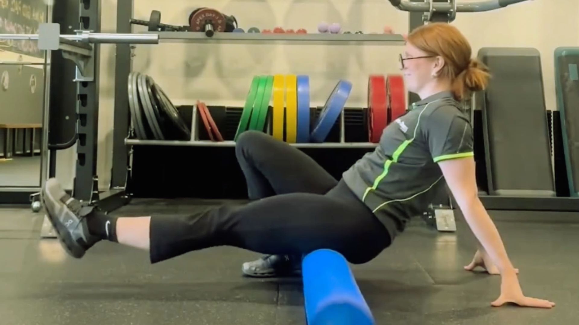 A woman performs a leg exercise on a foam roller, focusing on balance and muscle stretching.