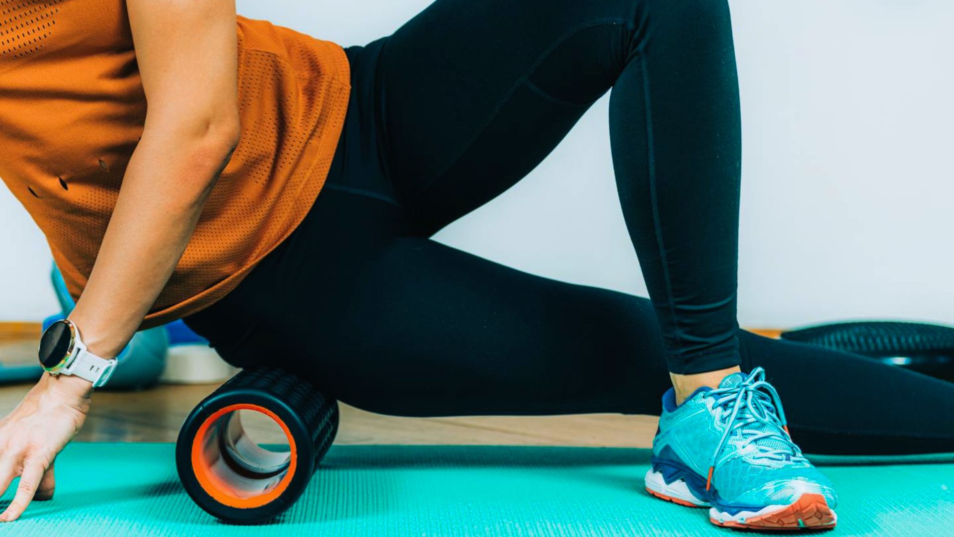 A woman sits on a foam roller, demonstrating a stretching or recovery exercise for muscle relief.