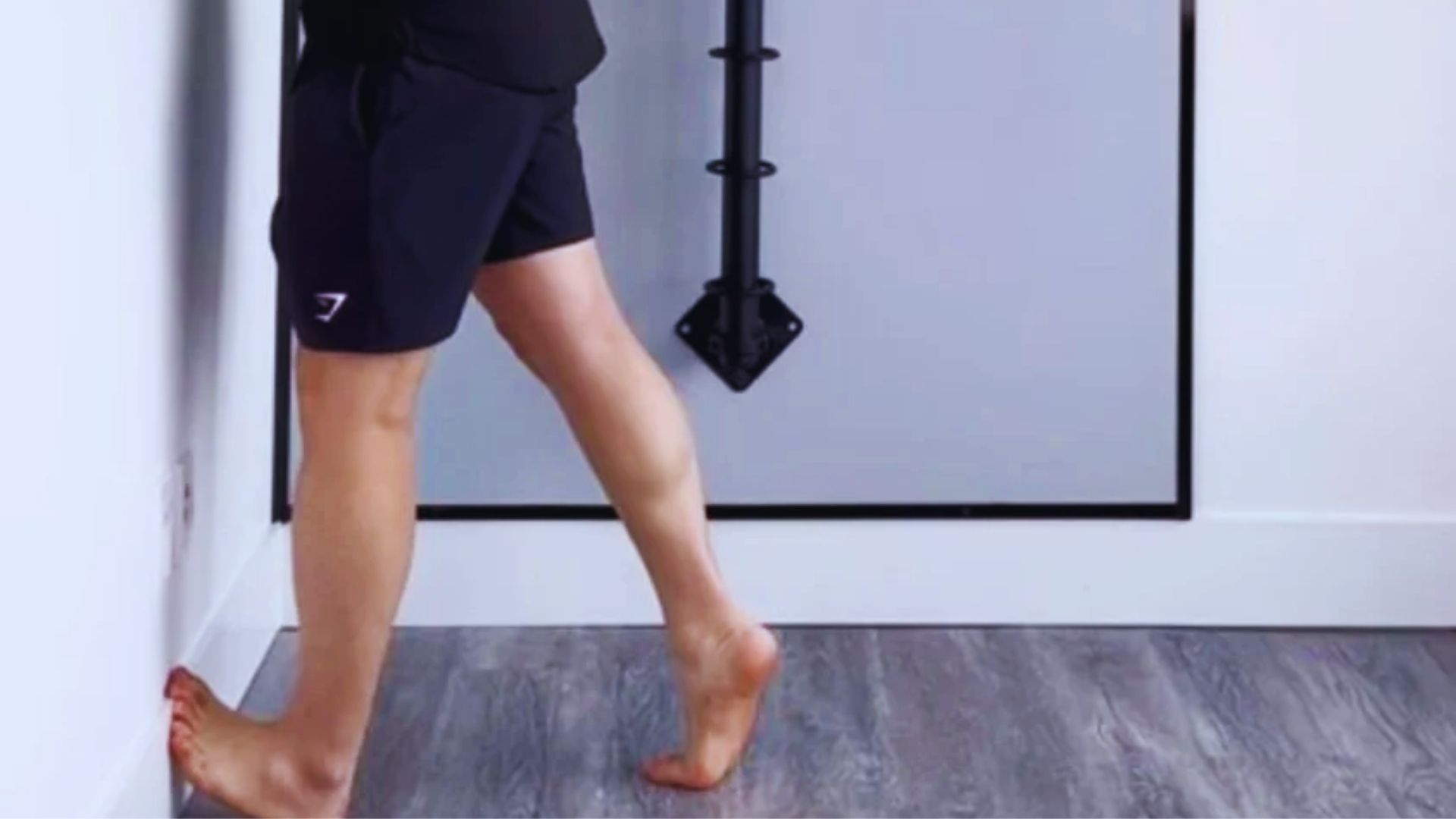 A person stands with one foot on a wall, creating a dynamic pose against the textured surface behind them.