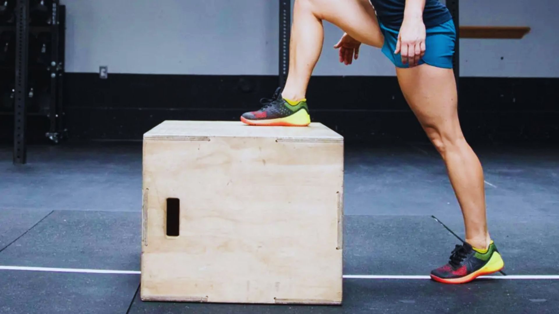 A woman performs a jump onto a sturdy box, showcasing her athleticism and strength during a workout session.