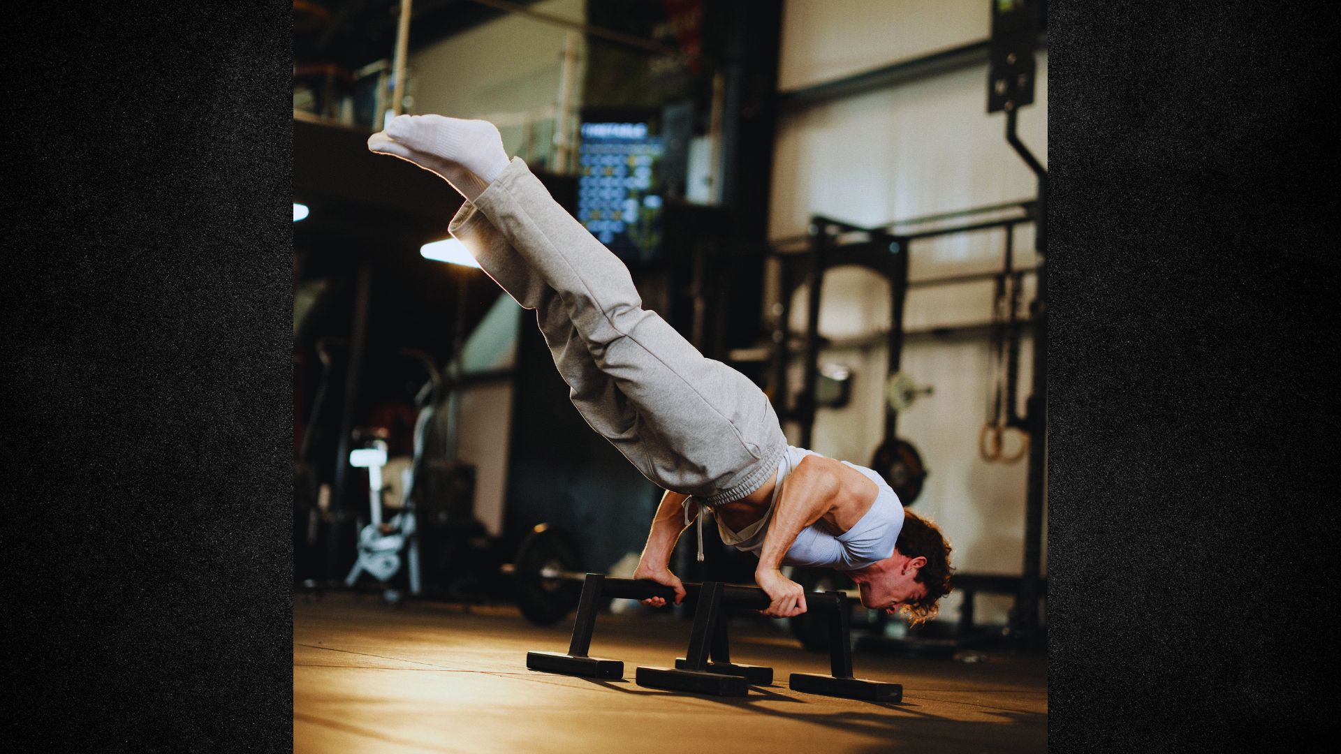 A man performing a handstand on a gym bar, showcasing strength and balance in a fitness environment.