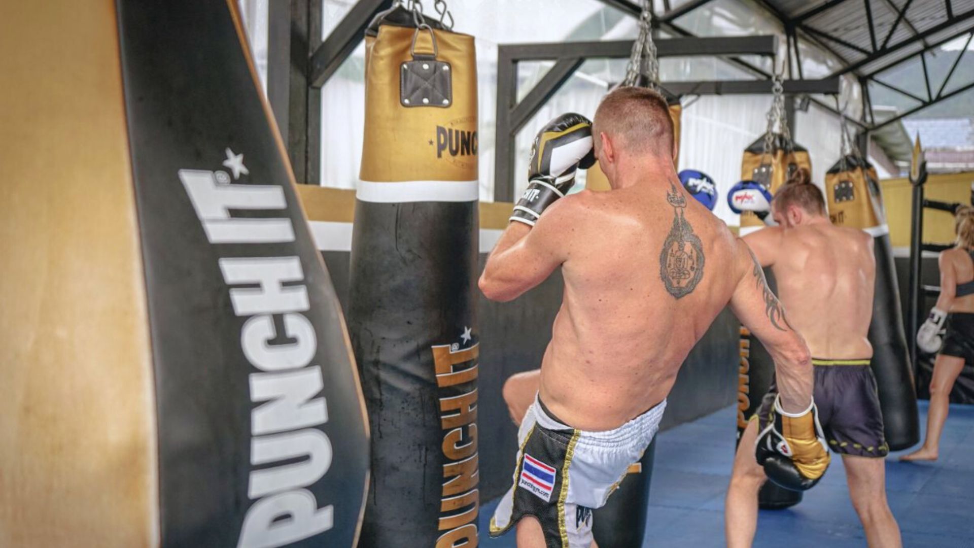A man stands in a boxing ring, preparing to strike a punching bag hanging in front of him.