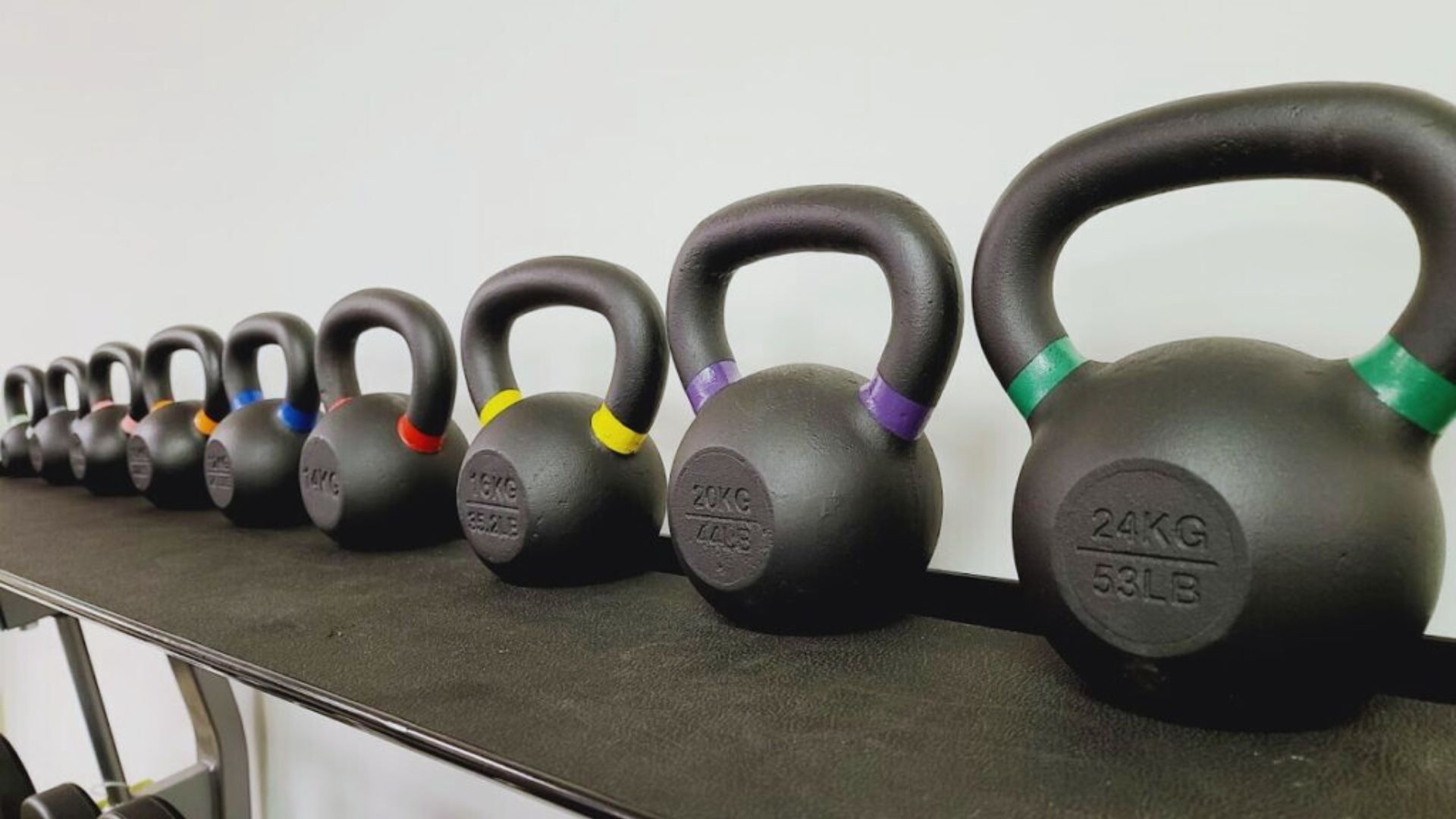 A row of colorful kettlebells neatly arranged on a shelf, showcasing various weights for strength training.