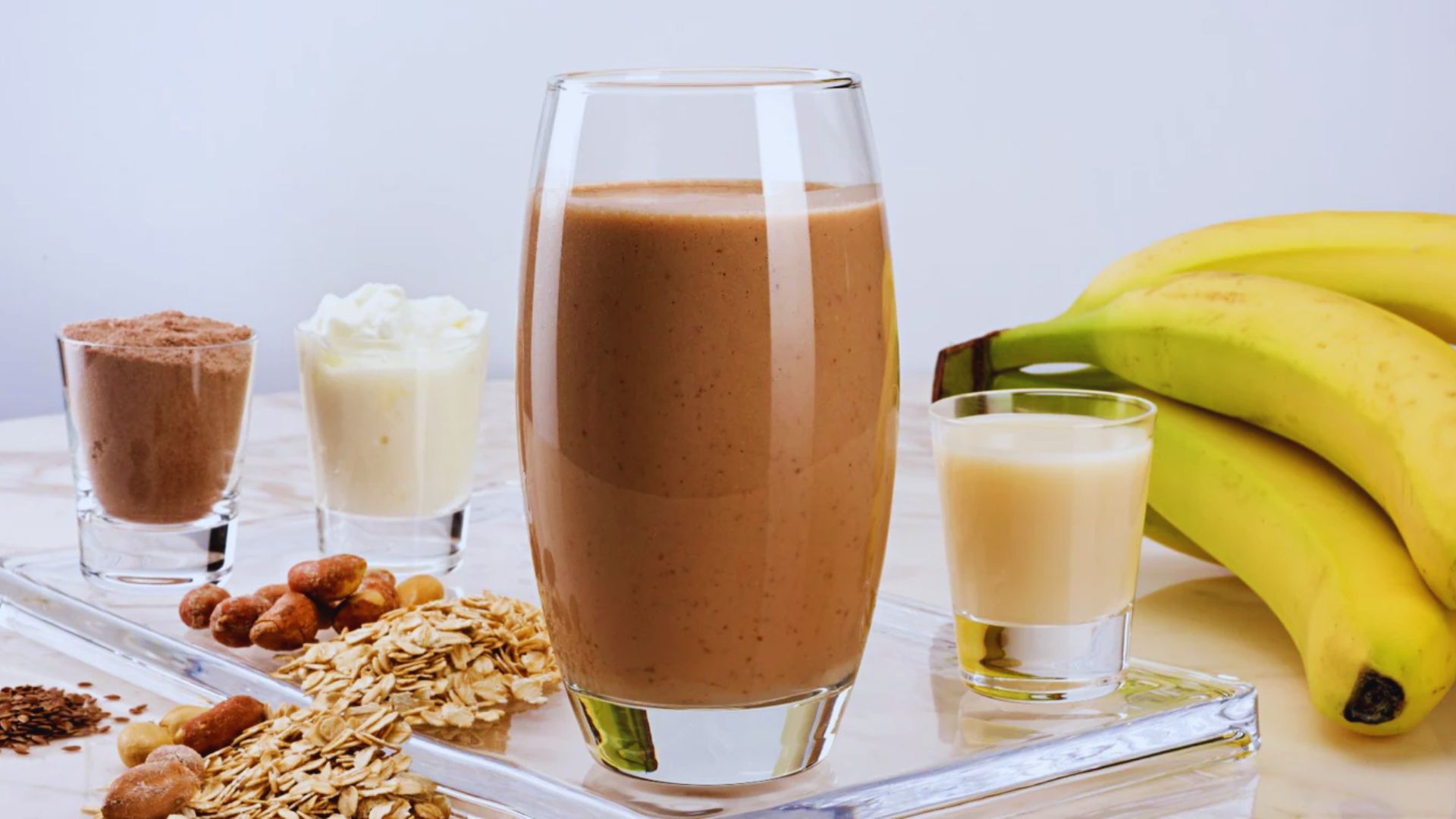 A glass of chocolate smoothie topped with banana slices and chopped nuts, placed on a wooden table.