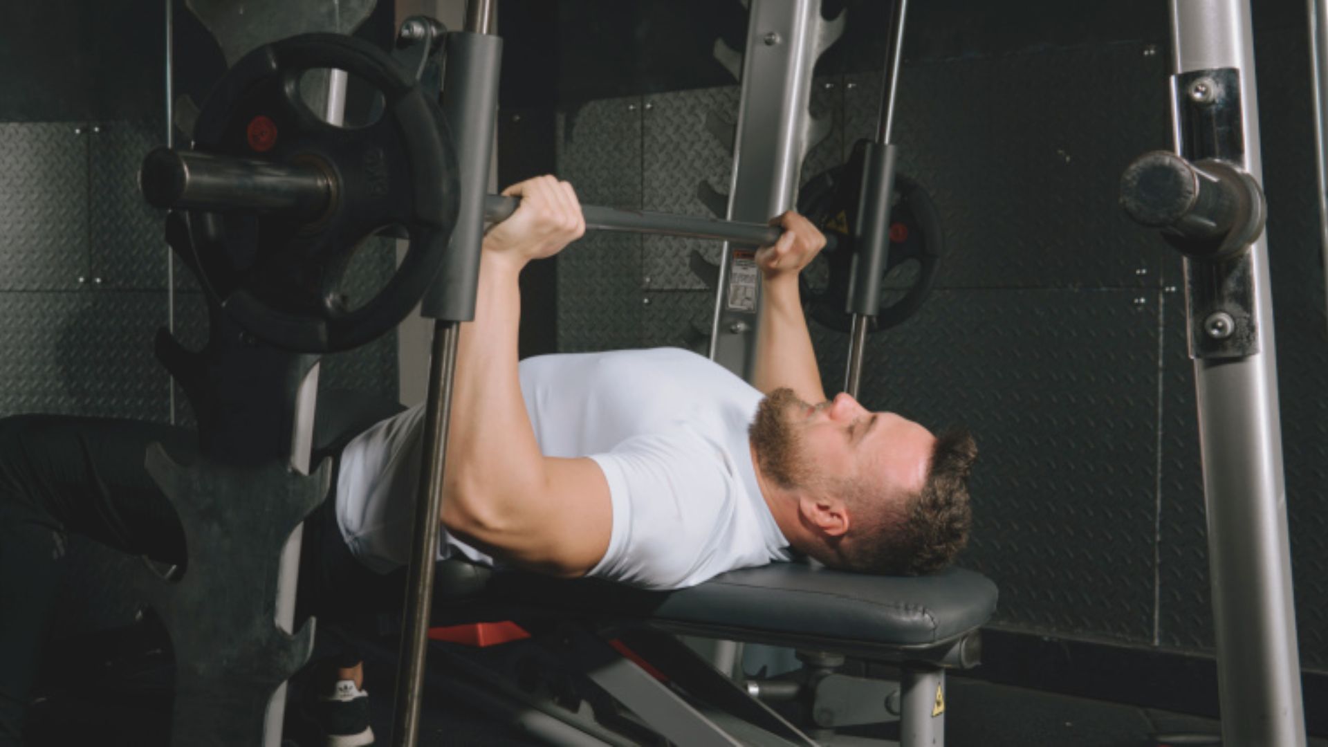 A man performs a bench press exercise in a gym, focusing on lifting a barbell above his chest.