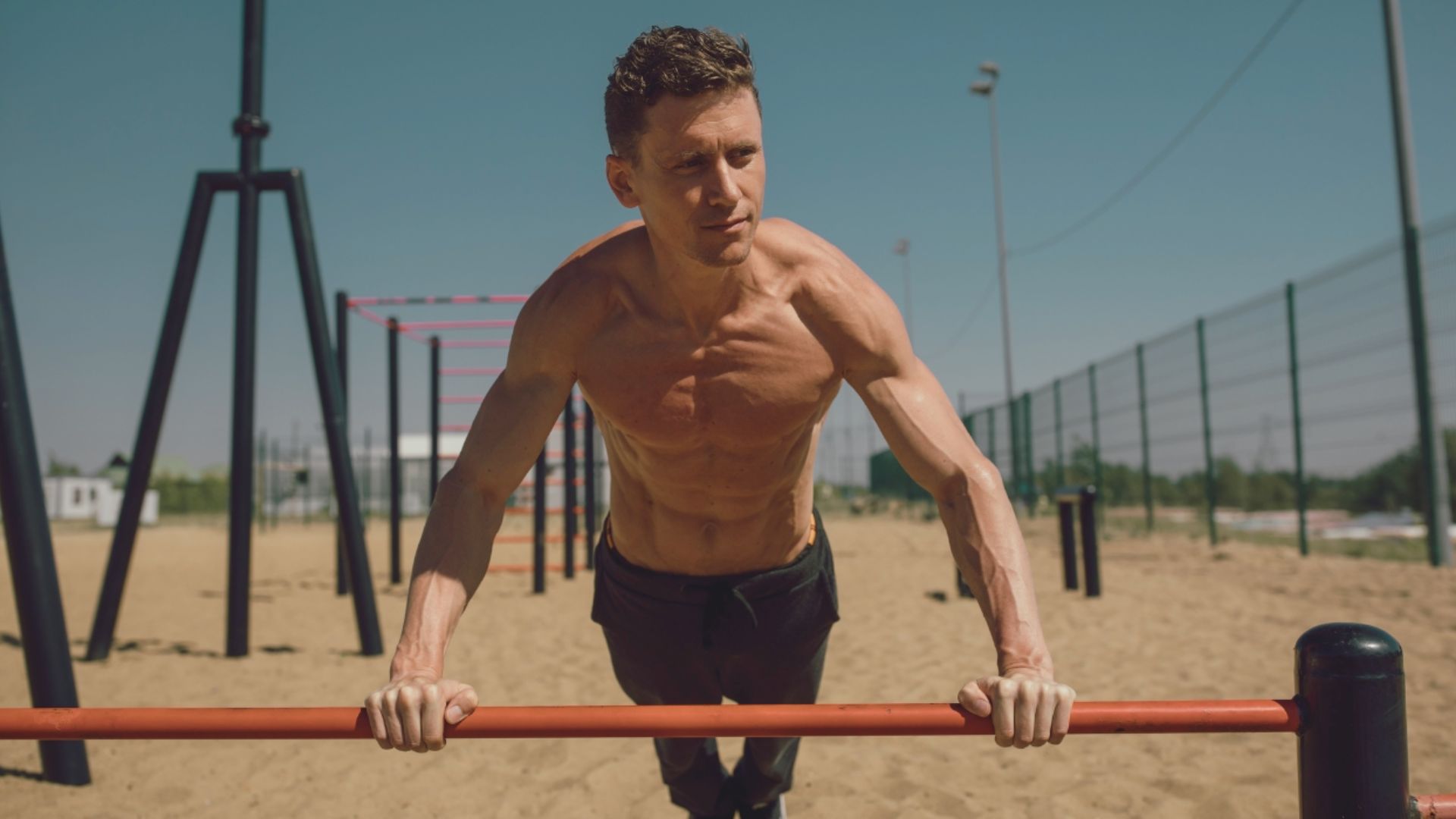 A shirtless man performing pull-ups on a bar, showcasing strength and athleticism in a fitness setting.