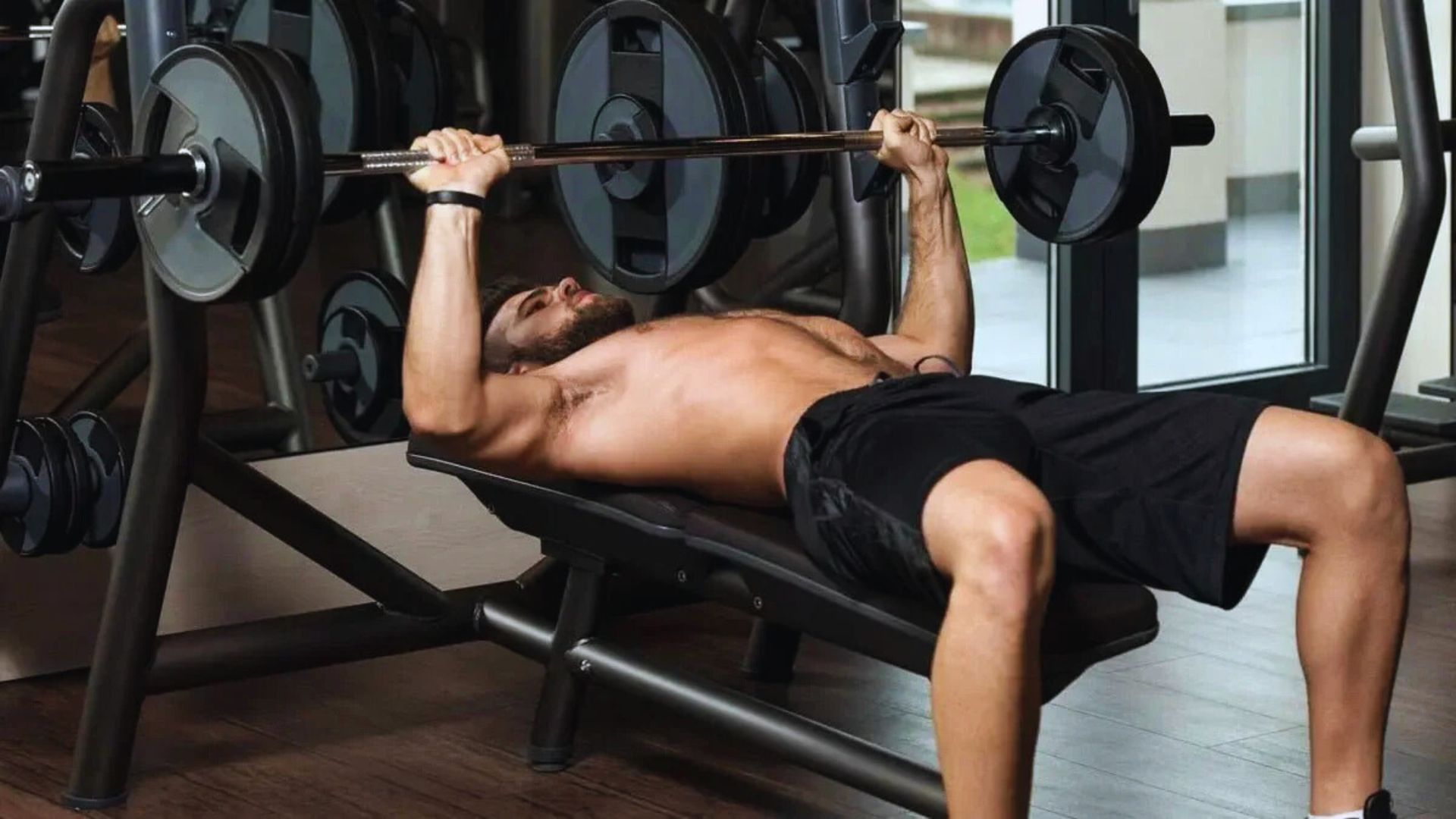 Man performing a bench press in a gym, lying on a bench, lifting a barbell with focused expression, embodying strength and determination.