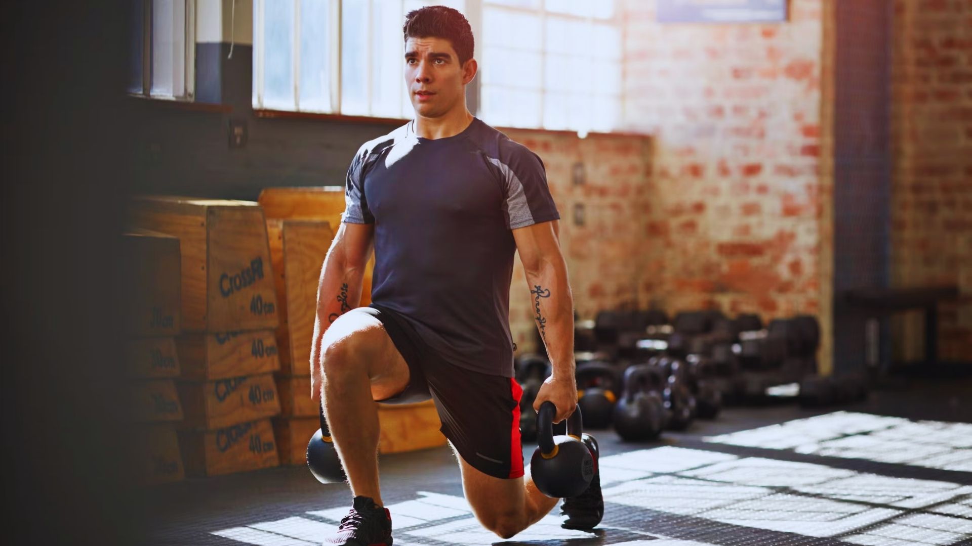 A man squats in a gym, holding a dumbbell in his right hand, focusing on his workout.