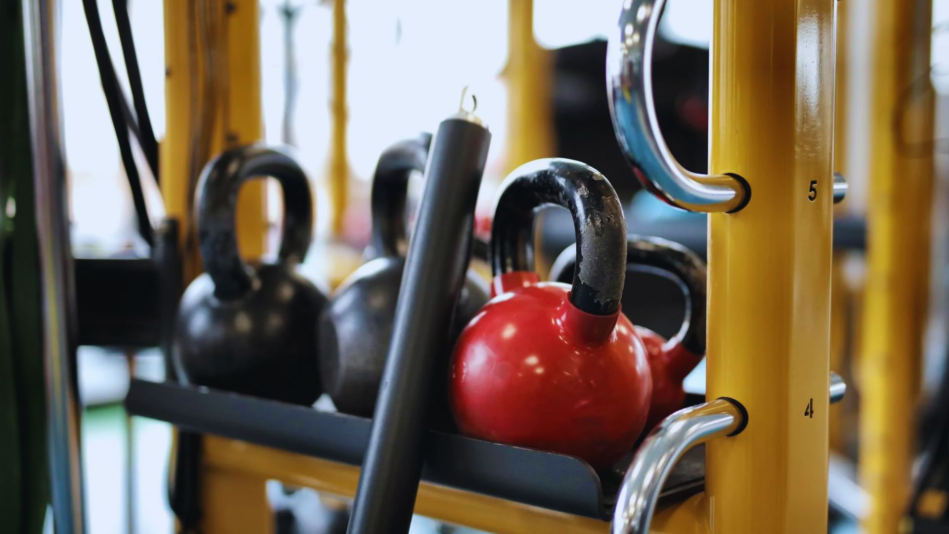 A variety of kettlebells arranged on a rack in a gym setting, showcasing different weights and colors.