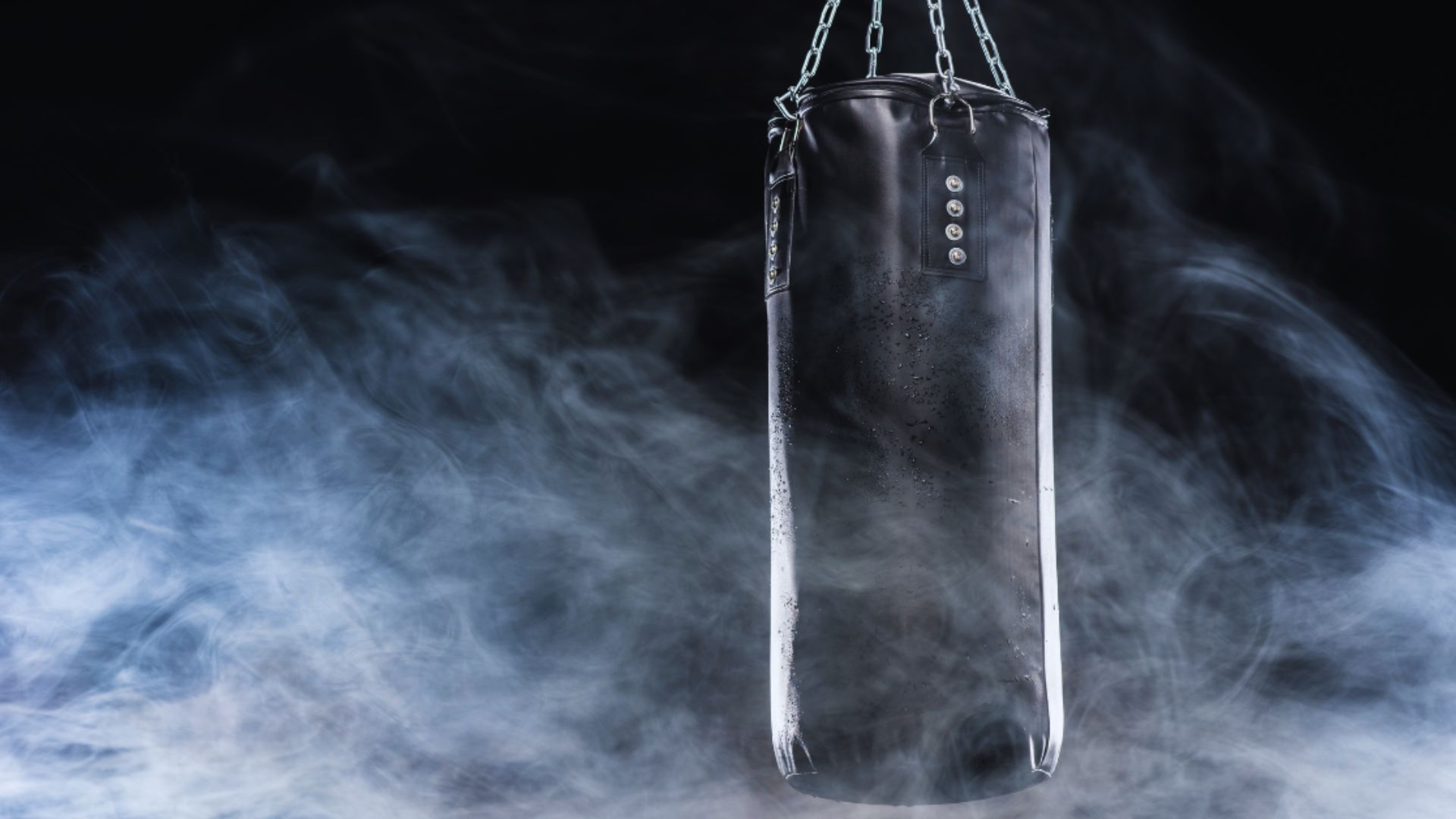 A boxing bag suspended in smoke against a dark black background, creating a dramatic and intense atmosphere.
