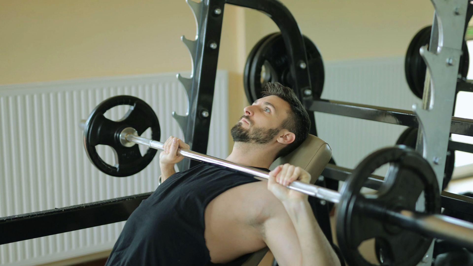 A man performs a bench press exercise in a gym, focusing on lifting a barbell above his chest.