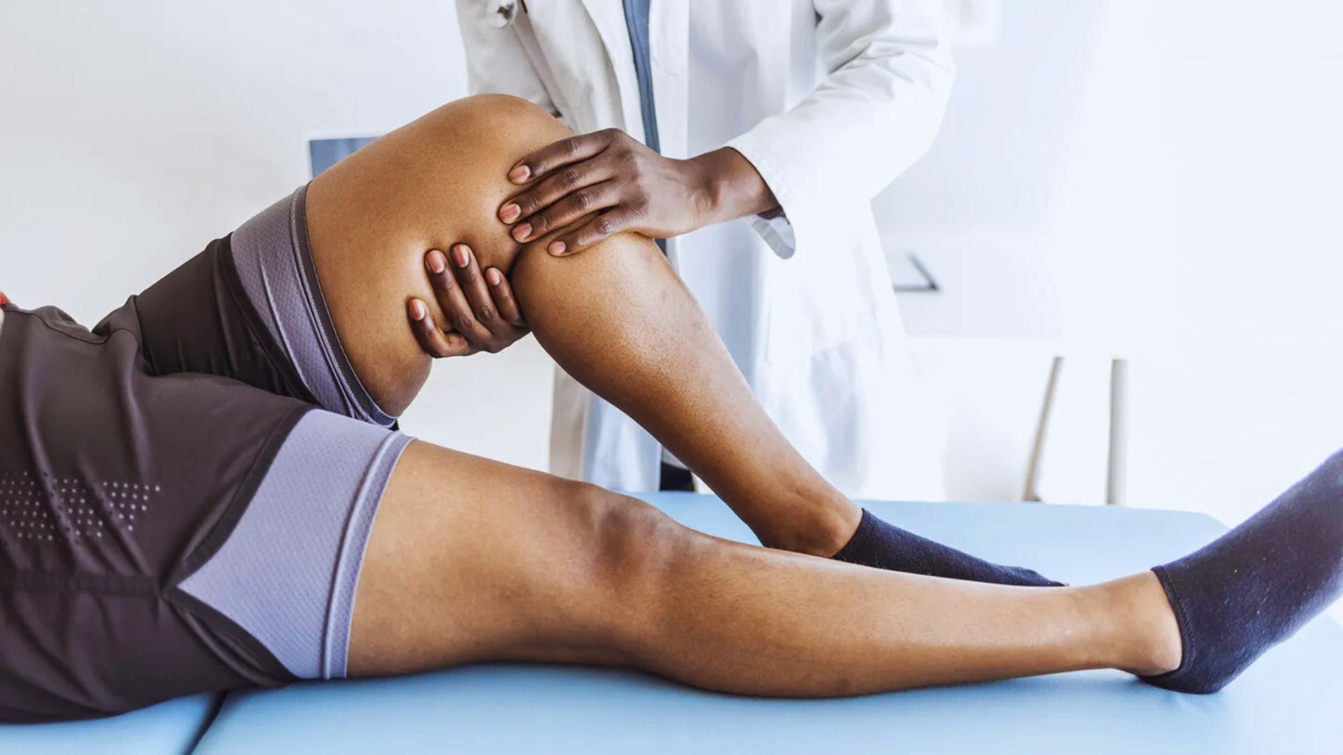 A physical therapist examines a patient's knee on a treatment table. The therapist's hands support the bent leg, conveying a sense of care and professionalism.