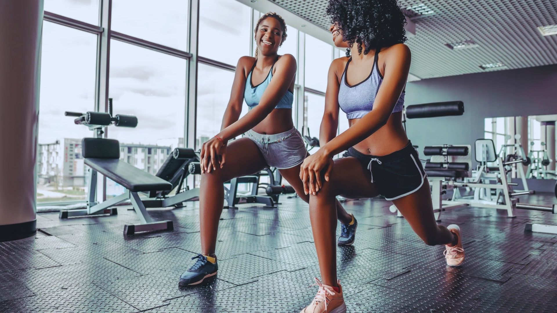 Two women performing squats in a gym, focusing on their form and strength training.