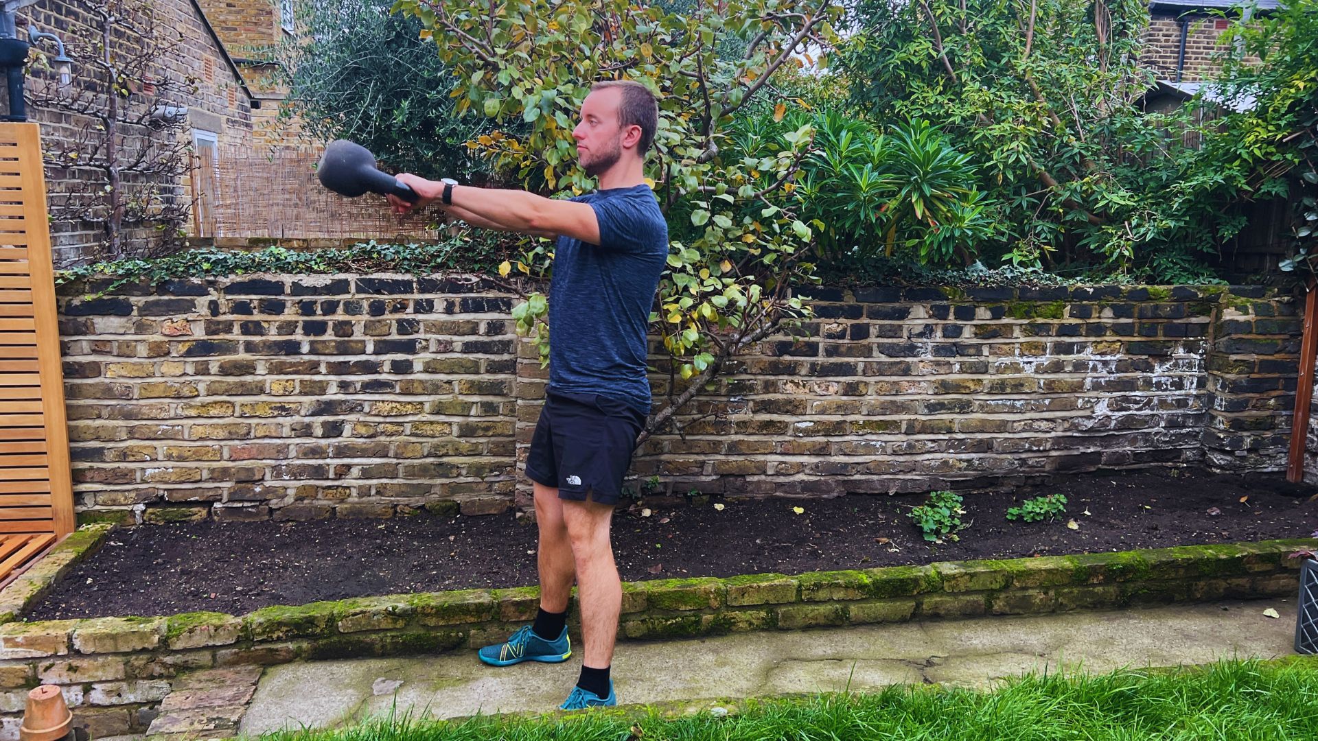 A man performs a kettlebell exercise in his backyard, showcasing strength and fitness in an outdoor setting.