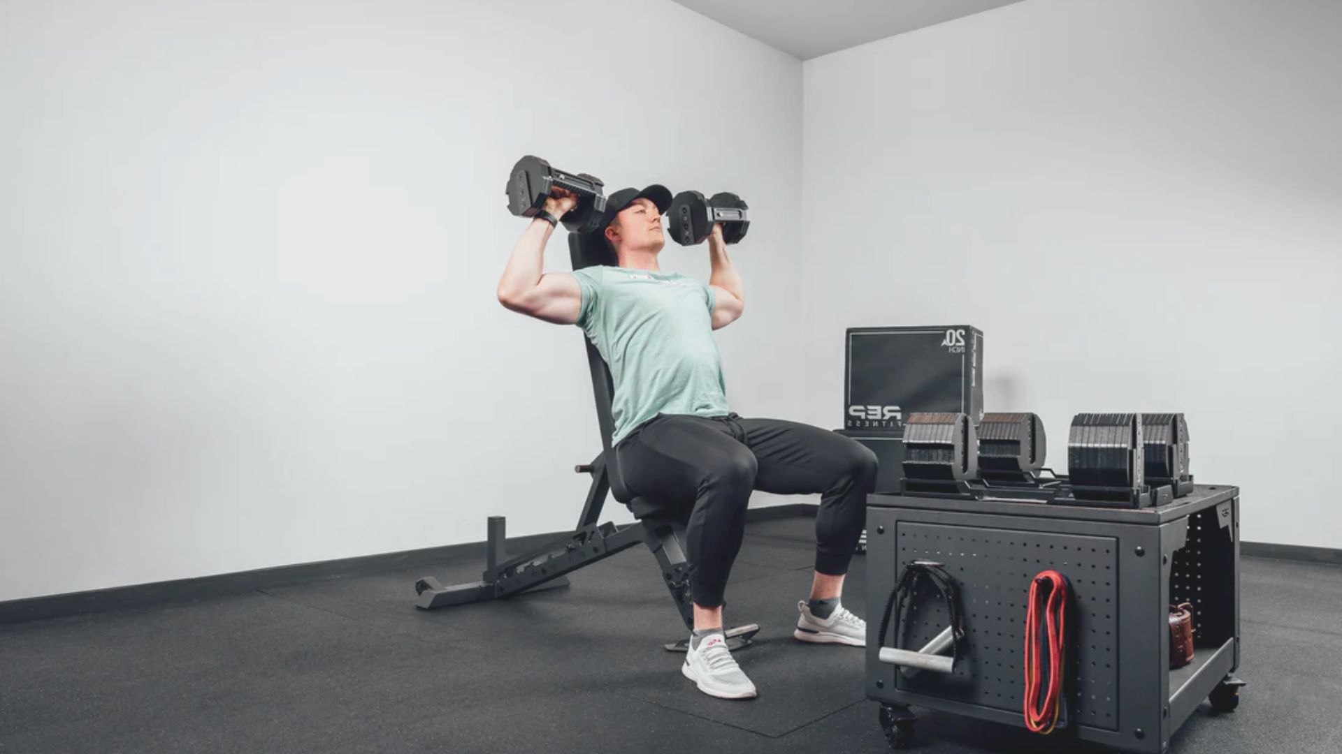 A man performs a bench press exercise using dumbbells in a gym setting.