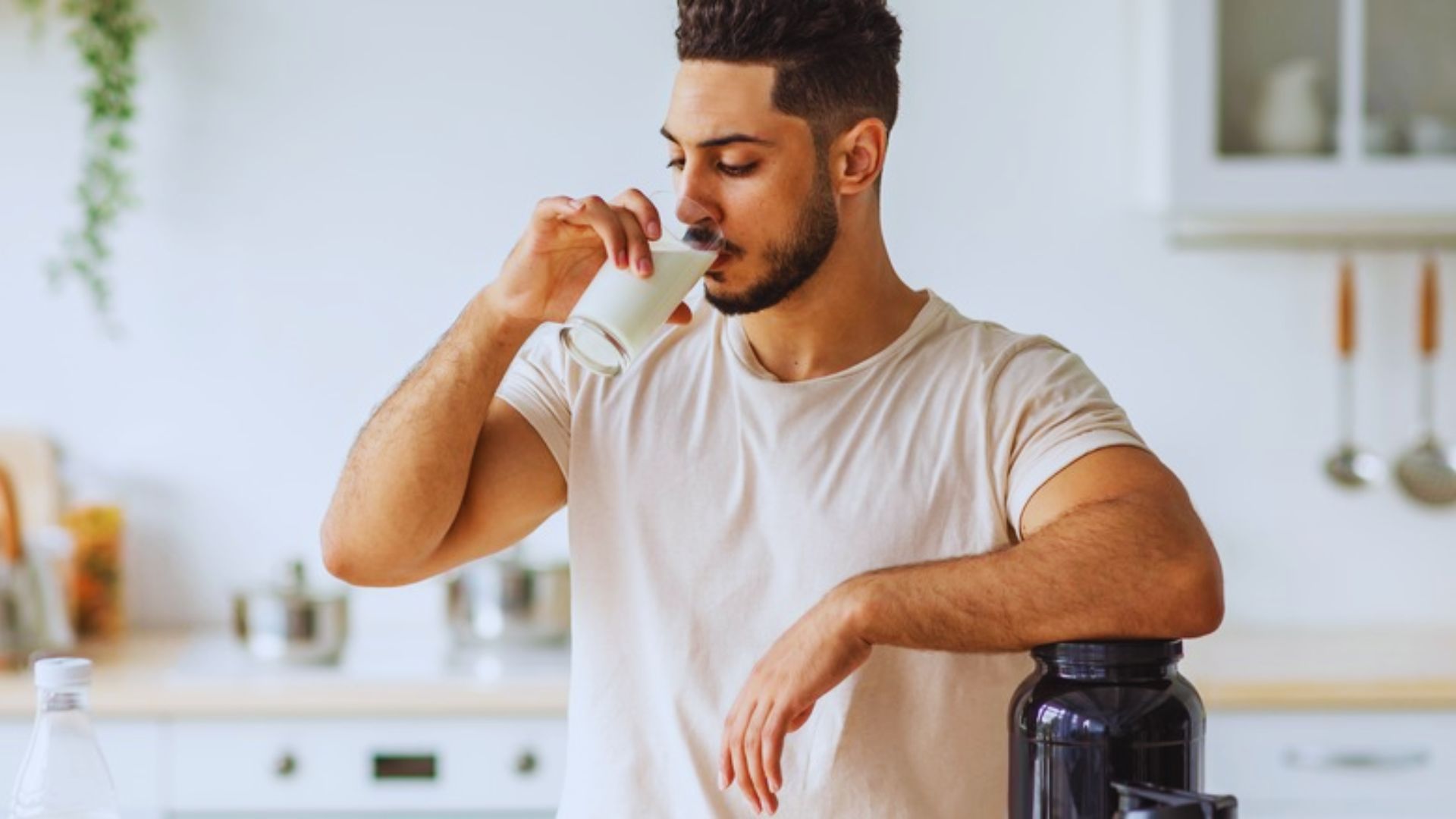 A man holding a glass, drinking milk with a focused expression.