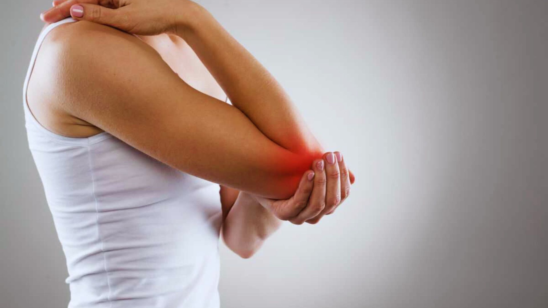 A person in a white tank top holds their elbow, which is highlighted in red, indicating pain or injury. The background is a neutral gray, conveying discomfort.