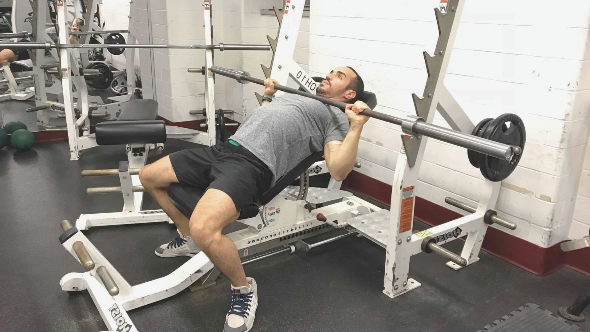 A man performs a bench press exercise in a gym, focusing on lifting a barbell above his chest.