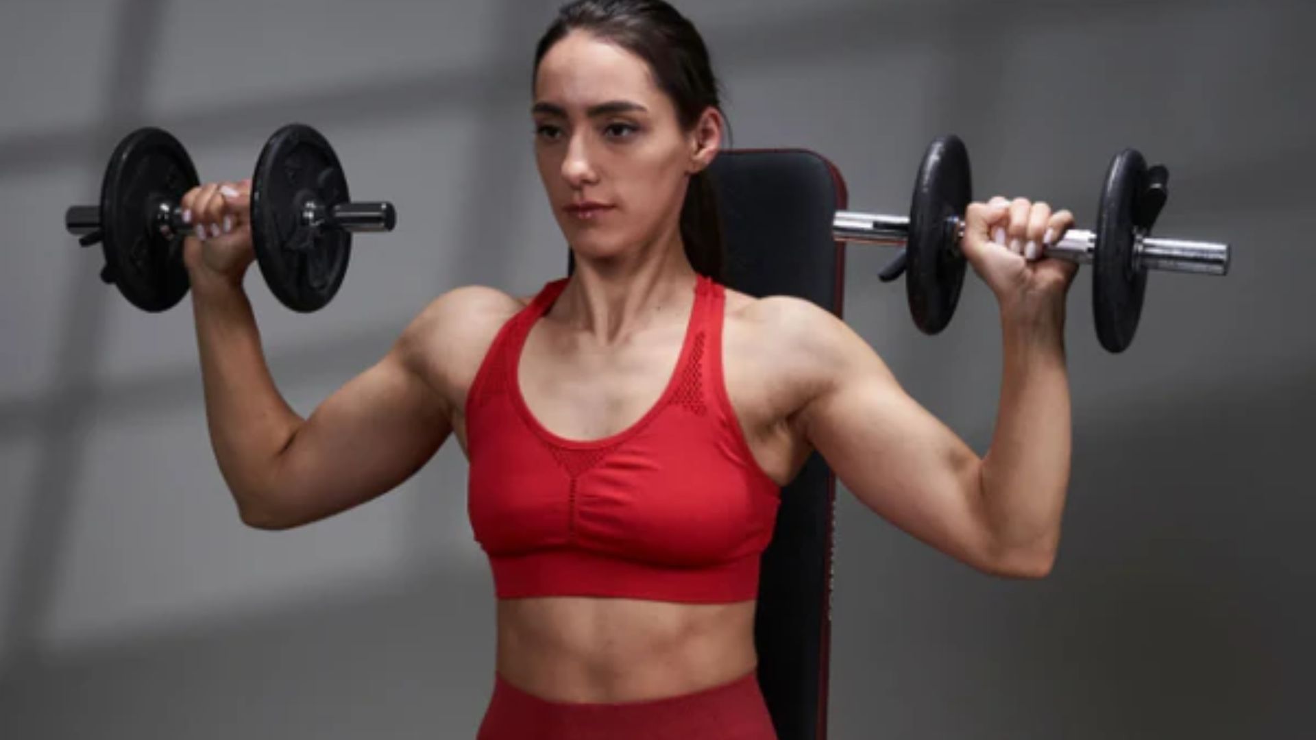 A woman in a red sports bra lifts weights, showcasing strength and determination in a fitness setting.