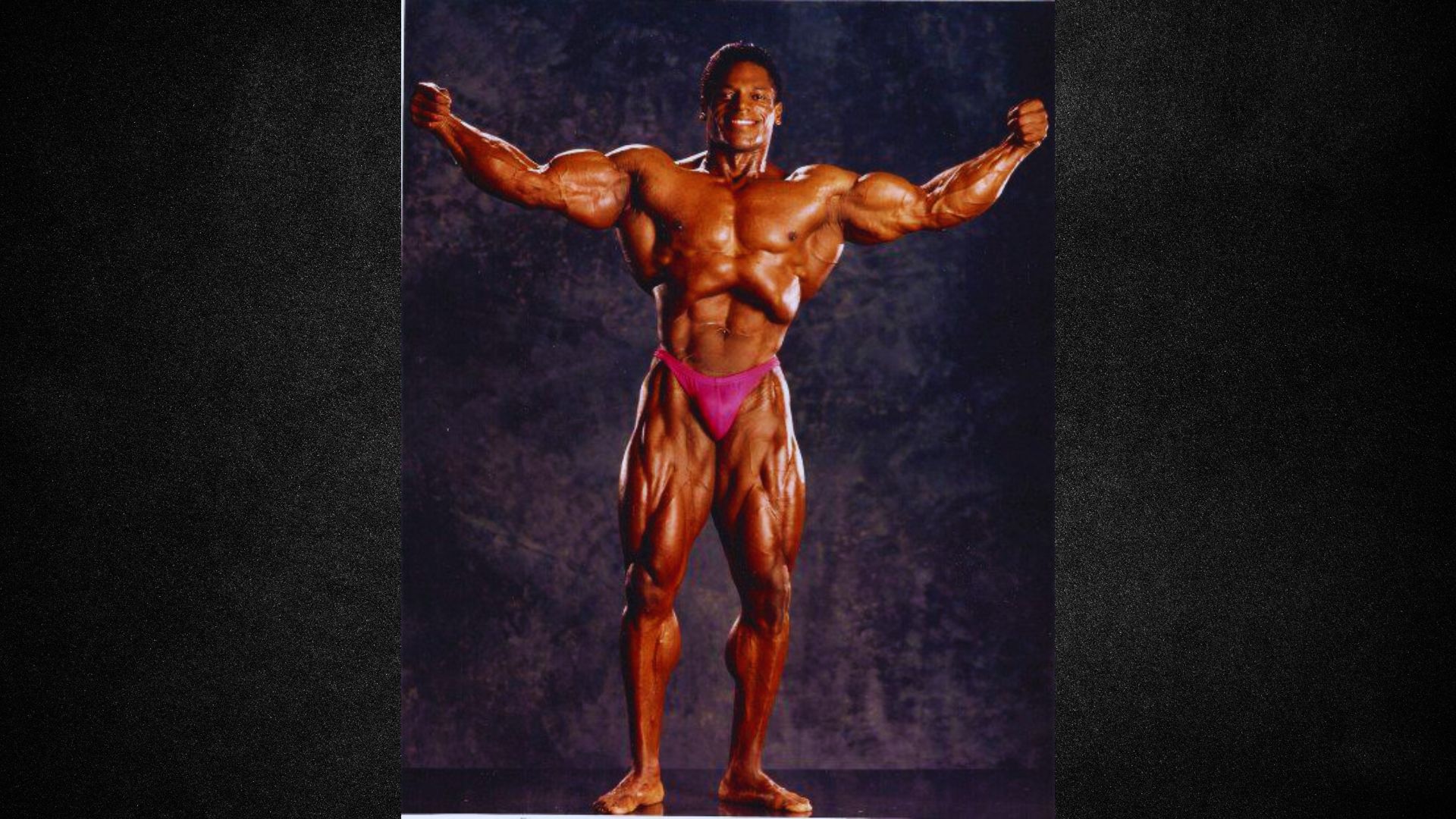 A man confidently poses on a bodybuilding stage, showcasing his physique and competing in a bodybuilding event.