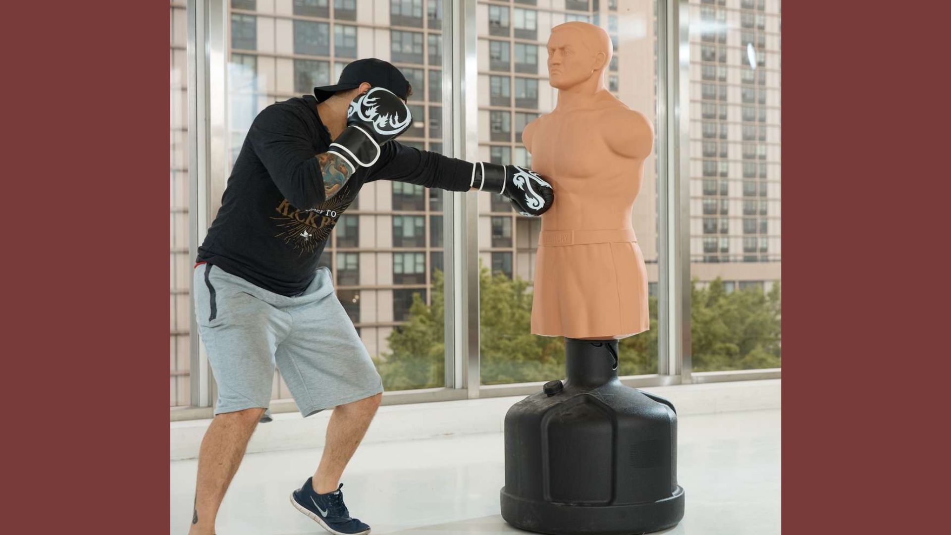A man practices boxing techniques with a training dummy in a gym setting.