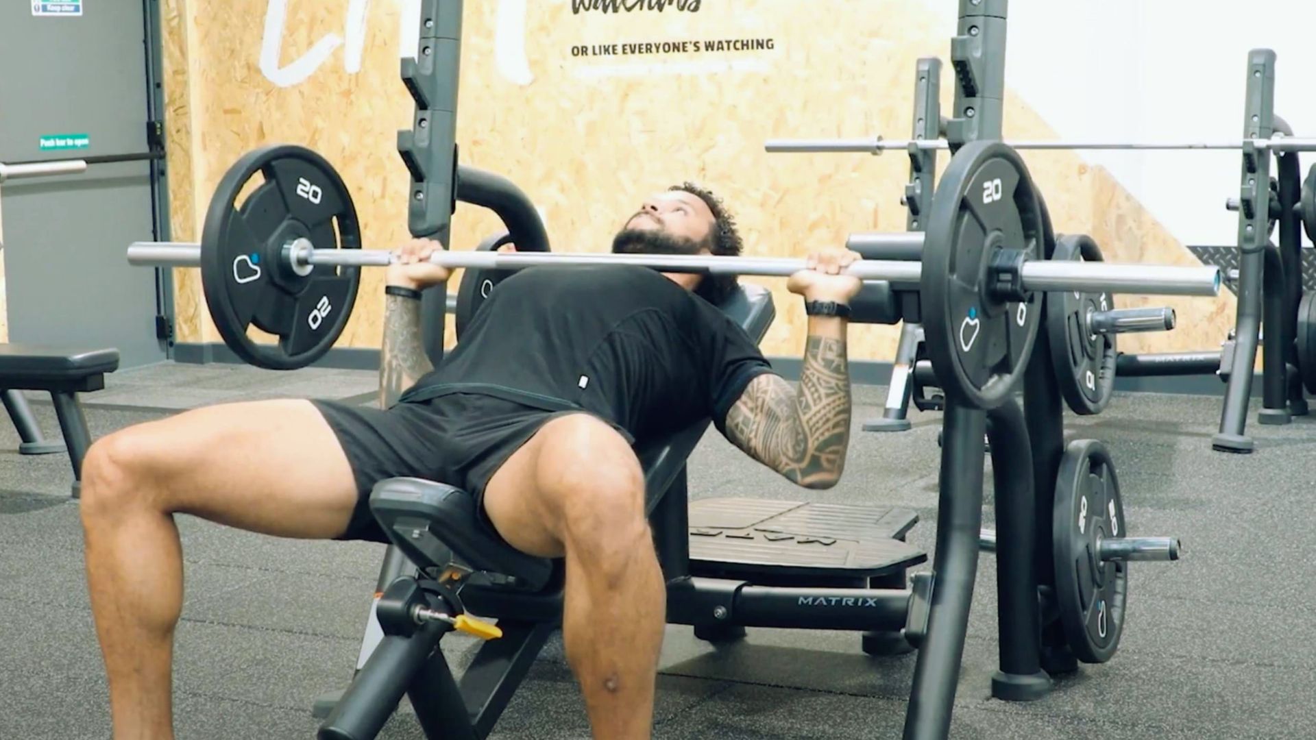 A man performs a bench press exercise in a gym, focusing on lifting a barbell above his chest.
