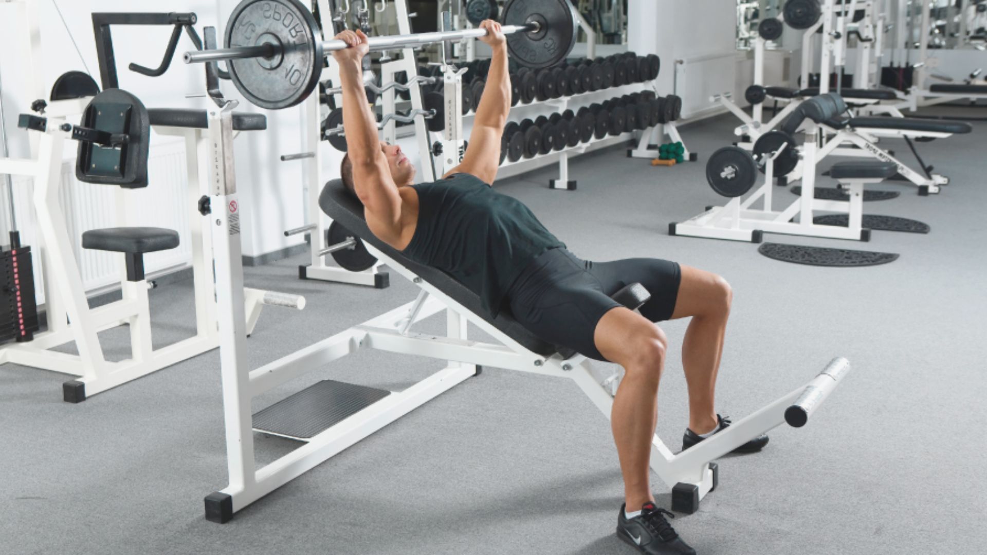 A man performs a bench press exercise in a gym, focusing on lifting a barbell above his chest.