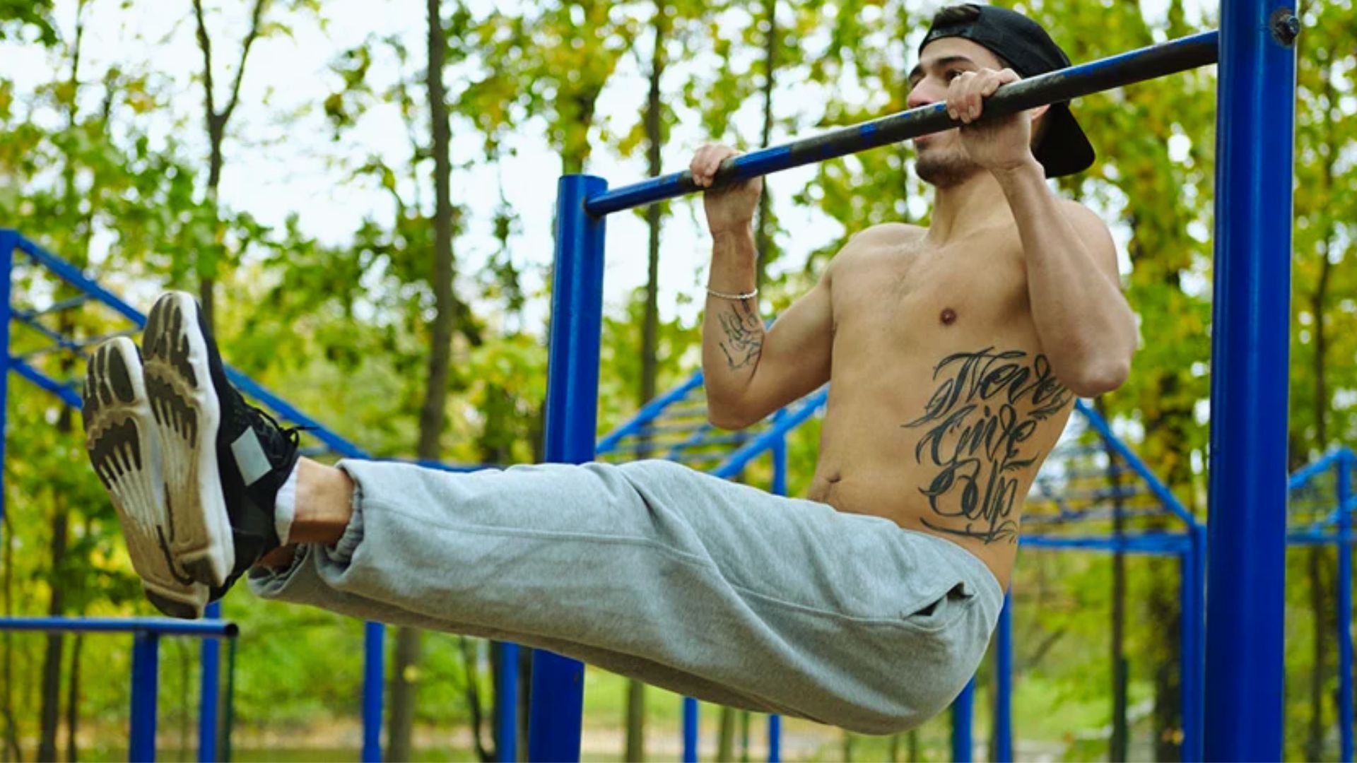 A man performs pull-ups using a park bench as support in a sunny outdoor setting.