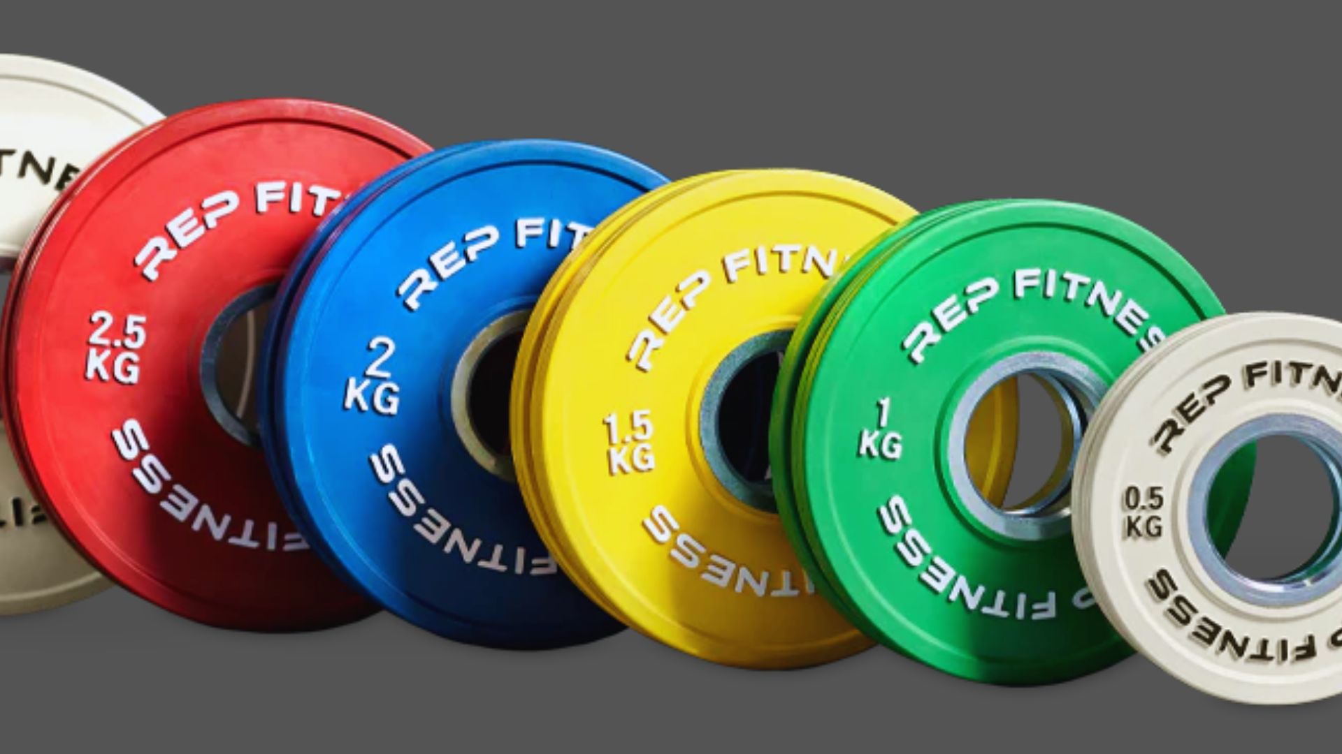 A set of colored weight plates arranged in a line against a gray background. Each plate displays "REP FITNESS" and varies in size and color, conveying a sense of fitness and training.