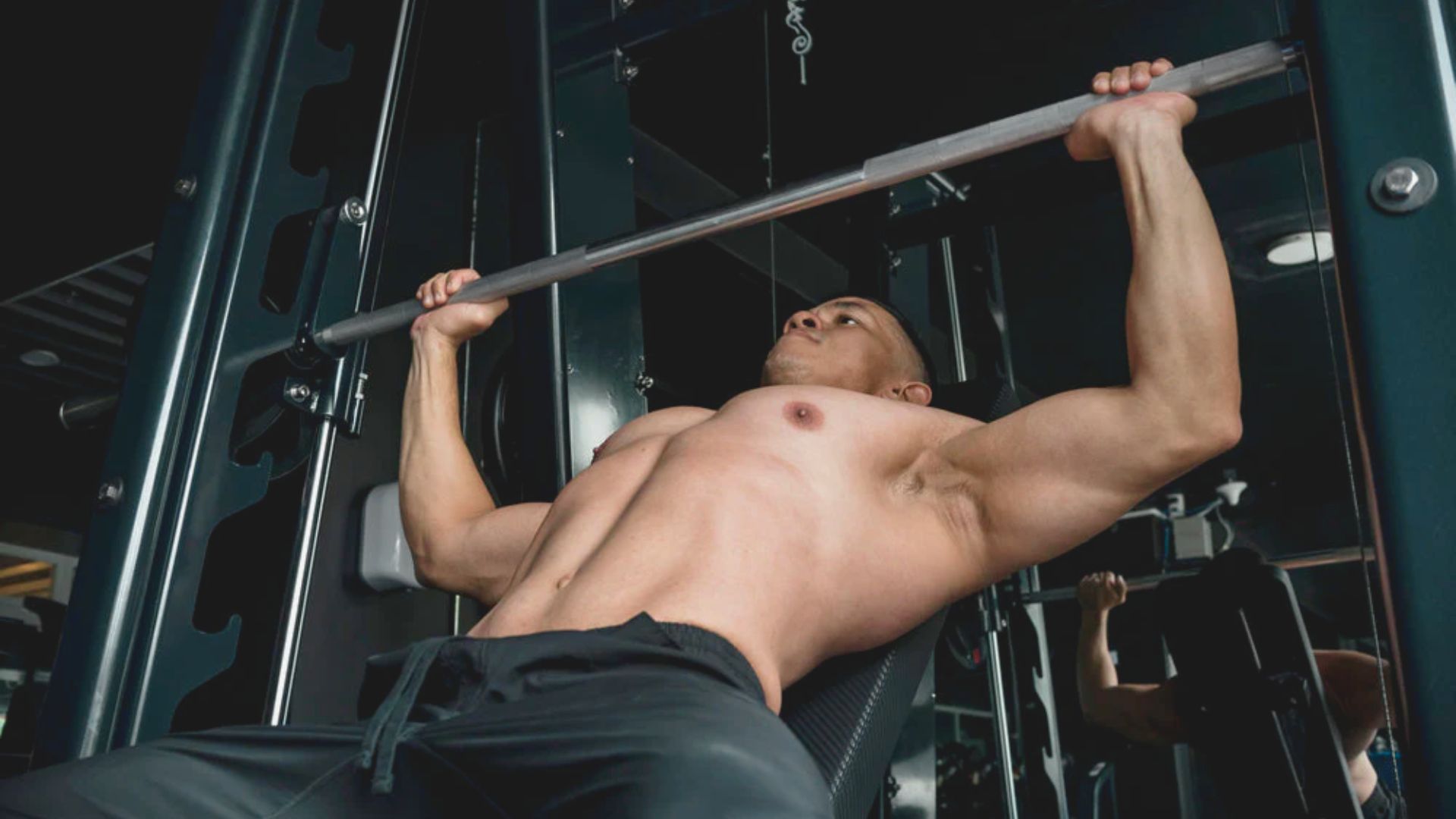 A man performs a pull-up on a bar, showcasing strength and fitness in a gym setting.