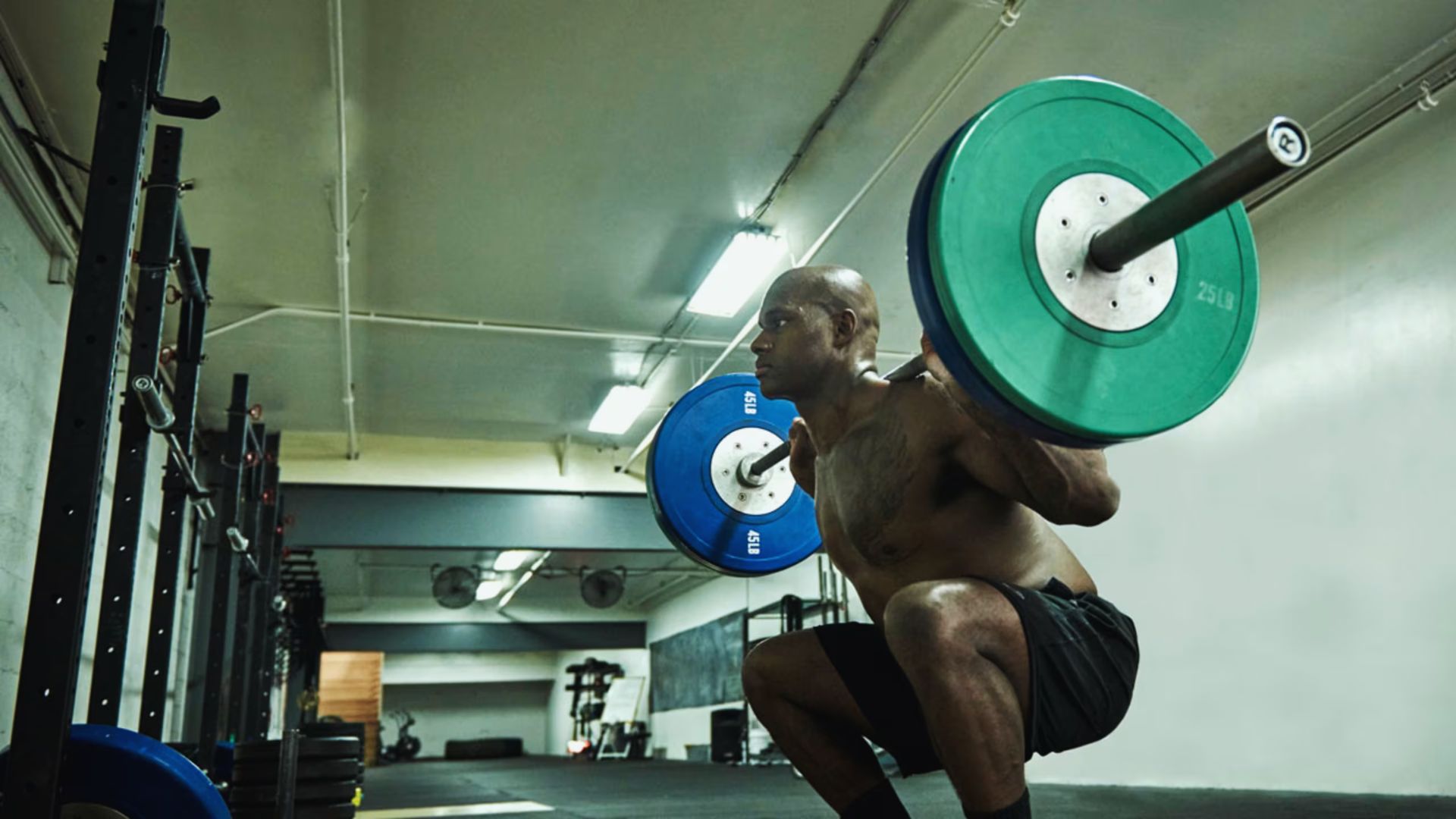 A person performs a squat with a heavy barbell in a gym. The focused expression and dimly lit space convey determination and strength.
