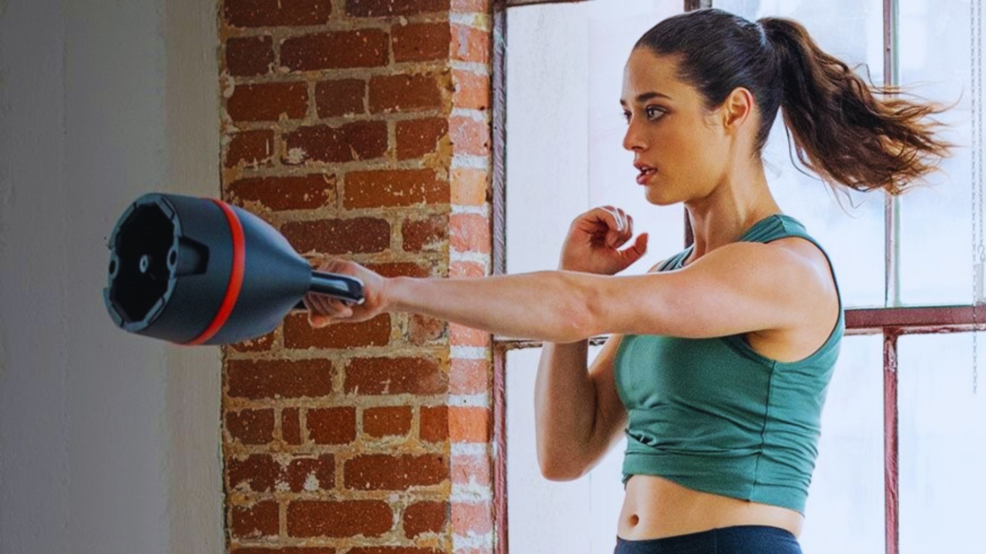 A woman holds a kettlebell in her hand, demonstrating strength and fitness in a workout setting.